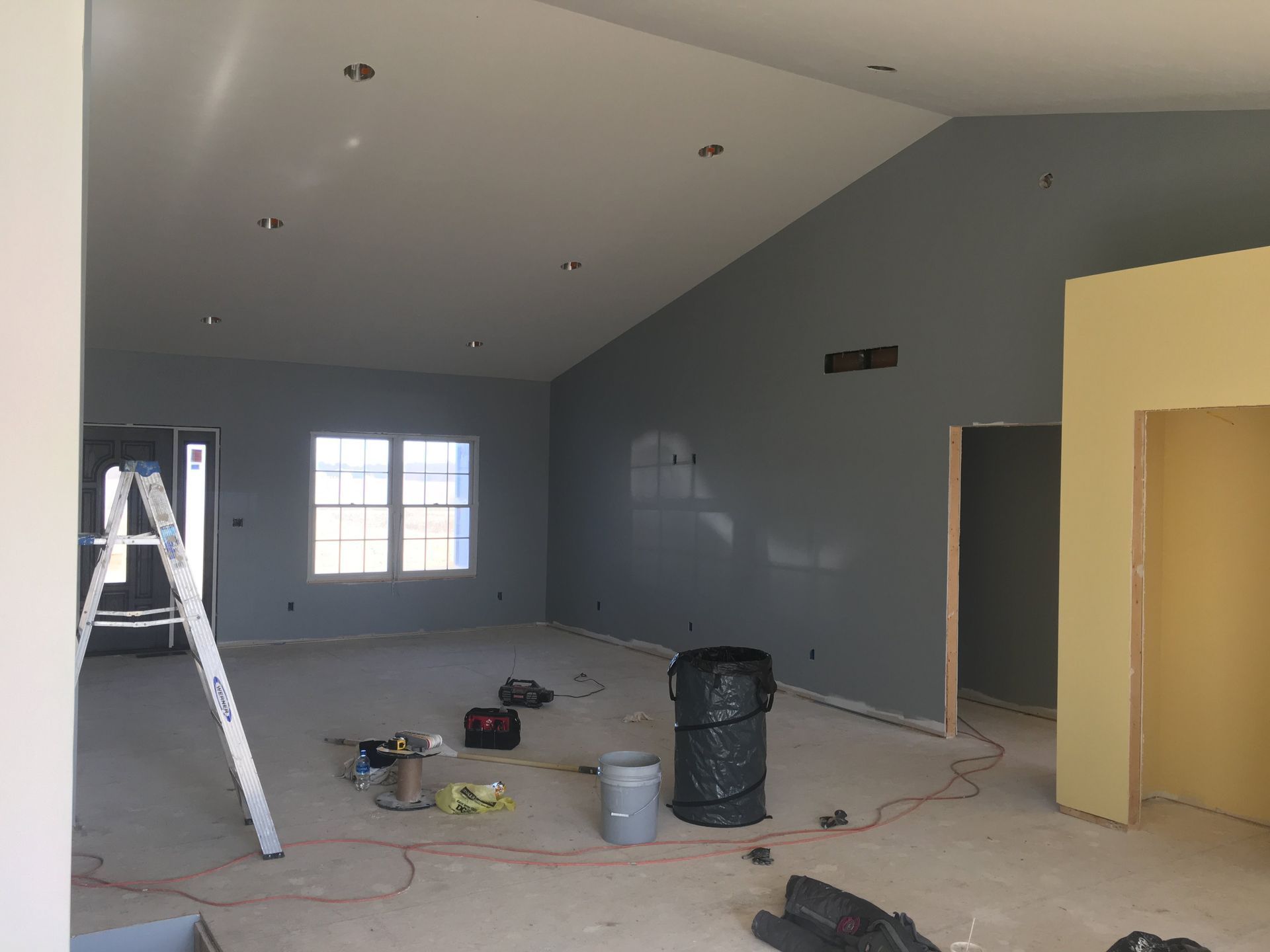 Interior of a room under renovation with gray walls, ladder, tools, and paint supplies on the floor