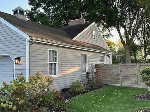 Gray house with white trim, side fence, green lawn, and trees in the yard