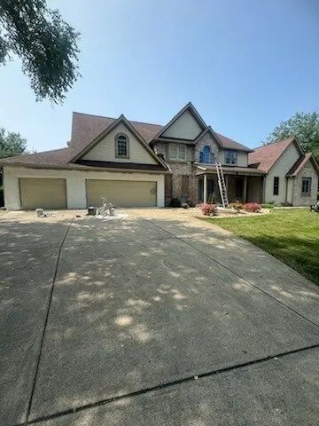 Suburban house with a three-car garage, driveway, and front porch under a clear blue sky