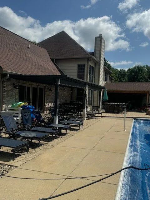 Backyard patio with lounge chairs beside a swimming pool and a house under a cloudy sky