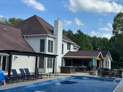 House with a backyard swimming pool and patio chairs under a partly cloudy sky