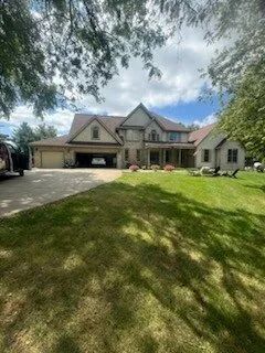 Large suburban house with a two-car garage, front porch, and green lawn under trees