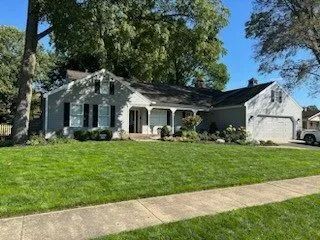 White suburban house with black shutters, front porch, green lawn, and concrete walkway under sunny sky