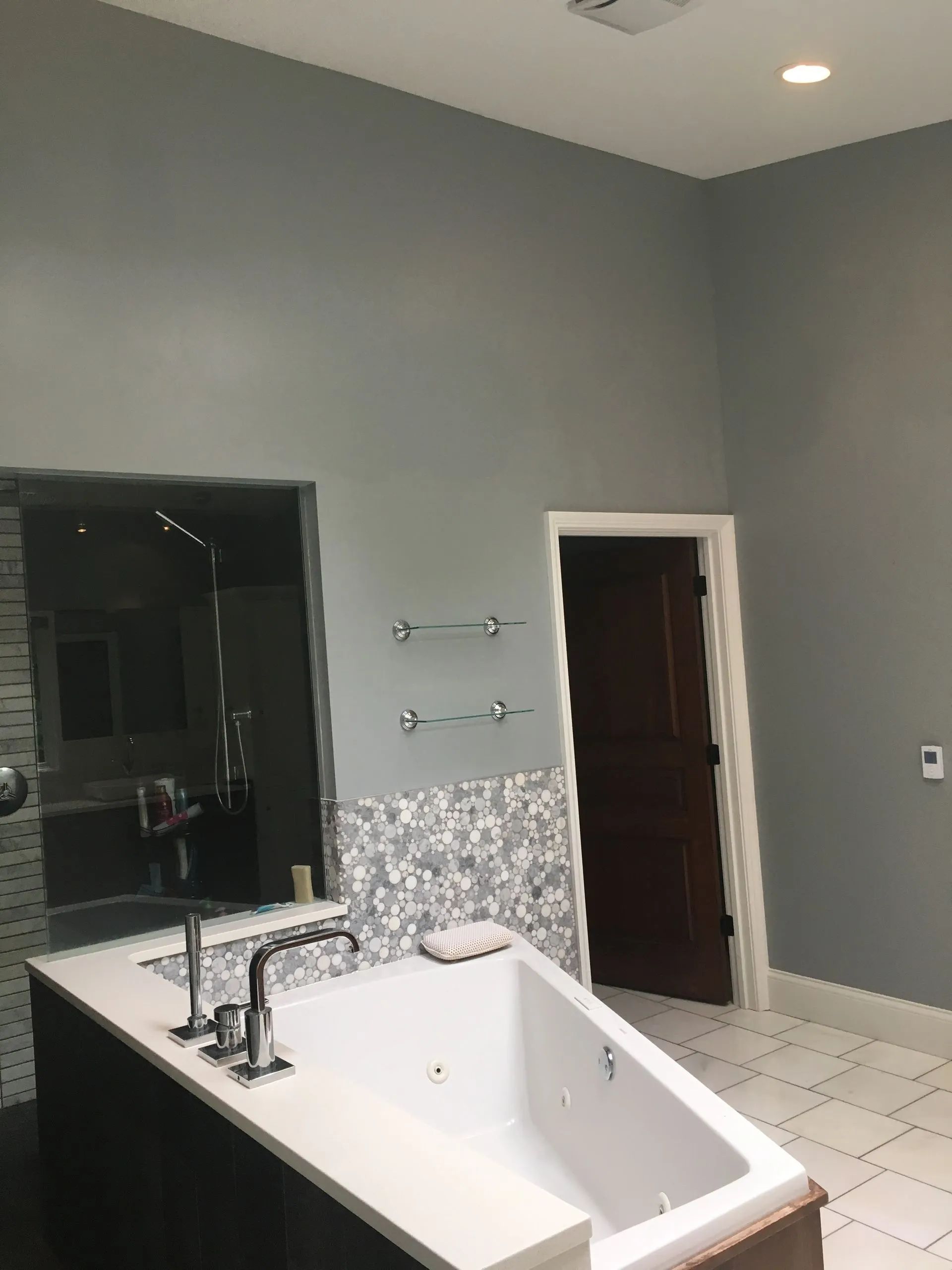 Modern bathroom with a white soaking tub, gray walls, and a large mirror beside a doorway.