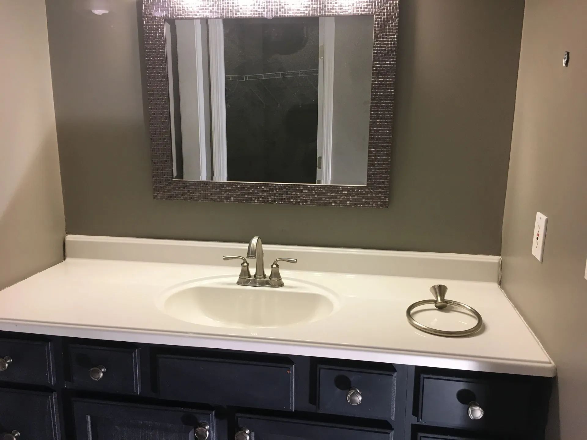 Bathroom vanity with white countertop, oval sink, mirror, and dark blue cabinets beneath.
