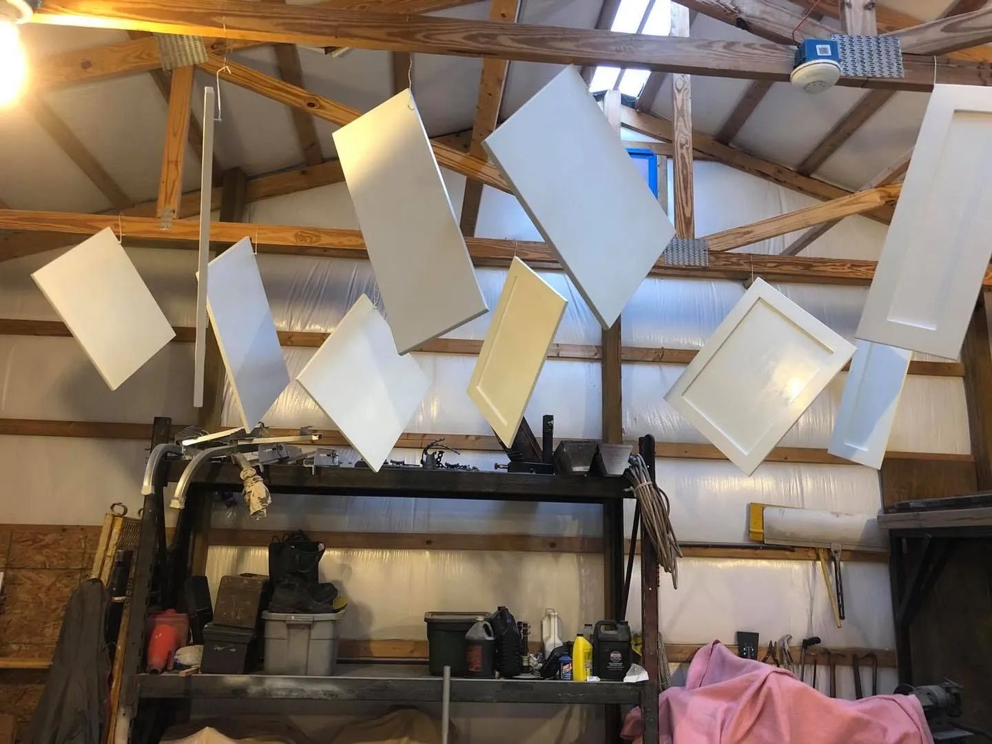 Workshop ceiling with hanging white rectangular panels and exposed wooden beams above shelves and tools