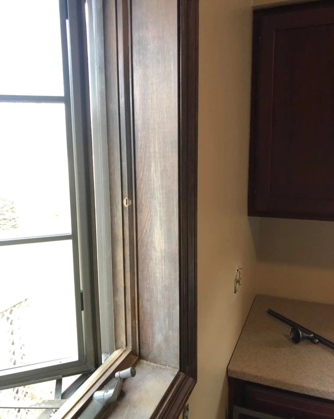 Open window beside a countertop and dark kitchen cabinet in a bright room.