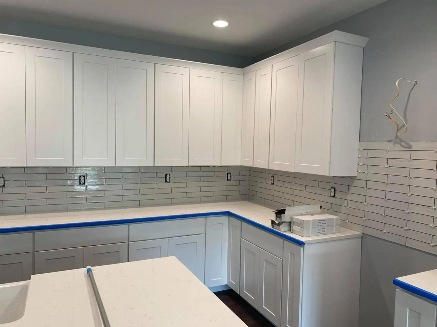 Bright white kitchen with gray tile backsplash, blue countertop edges, and white cabinets
