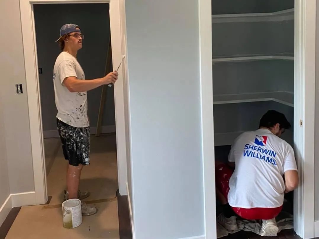 Two workers installing shelving in a small closet and doorway area during home renovation