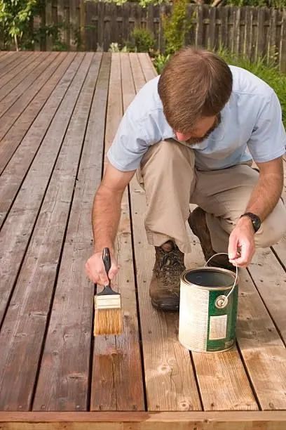 Person staining a wooden deck with a brush and paint can outdoors