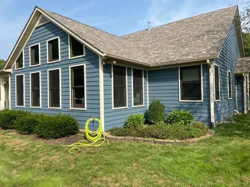 Blue house exterior with white trim, black shutters, and a green lawn under a clear sky