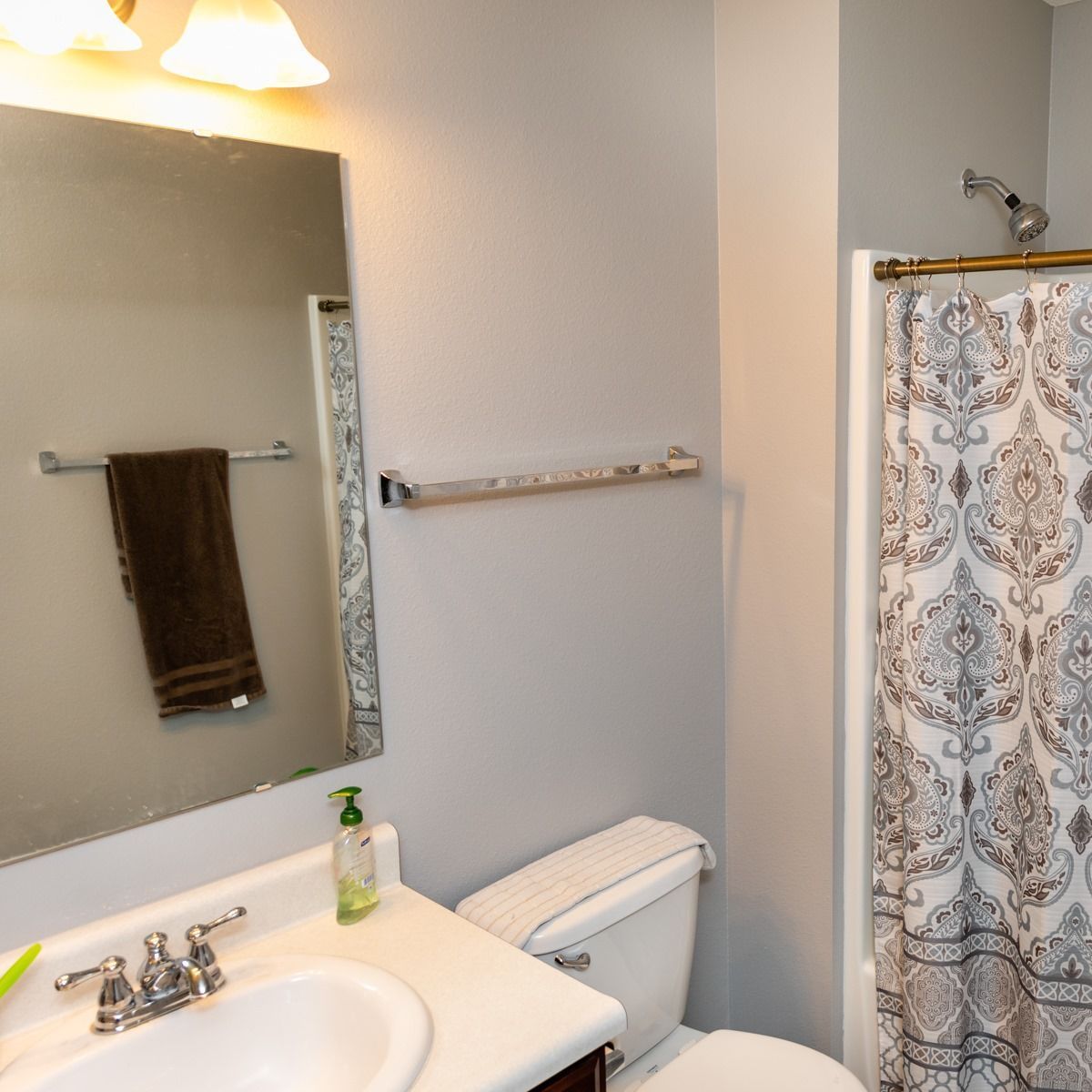Bathroom with sink, mirror, toilet, towel rack, and patterned shower curtain