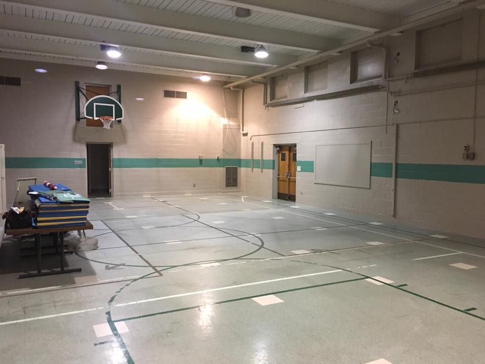 Empty indoor gym with basketball hoop and folding tables along the left wall