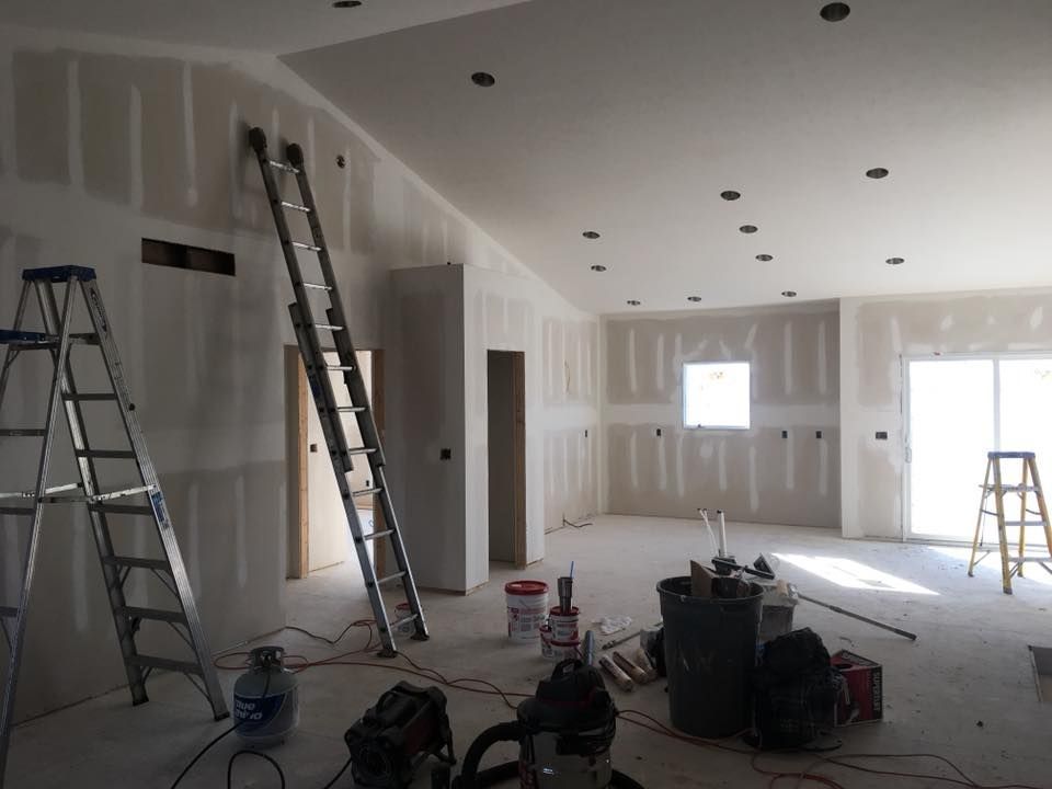 Unfinished room under construction with drywall, ladders, tools, and light from windows and a door.