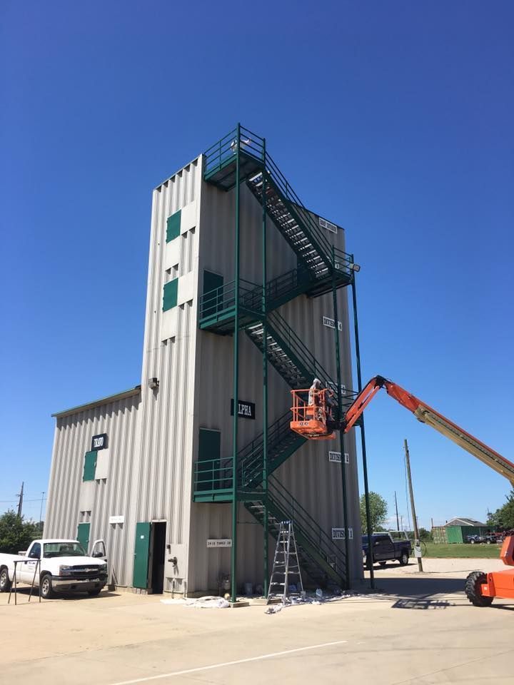 Industrial training tower with exterior stairs and a boom lift under a clear blue sky