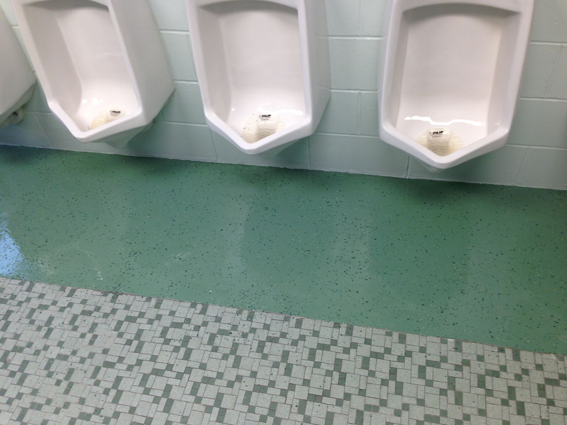 Three white urinals on a mint-green bathroom wall above a tiled floor.