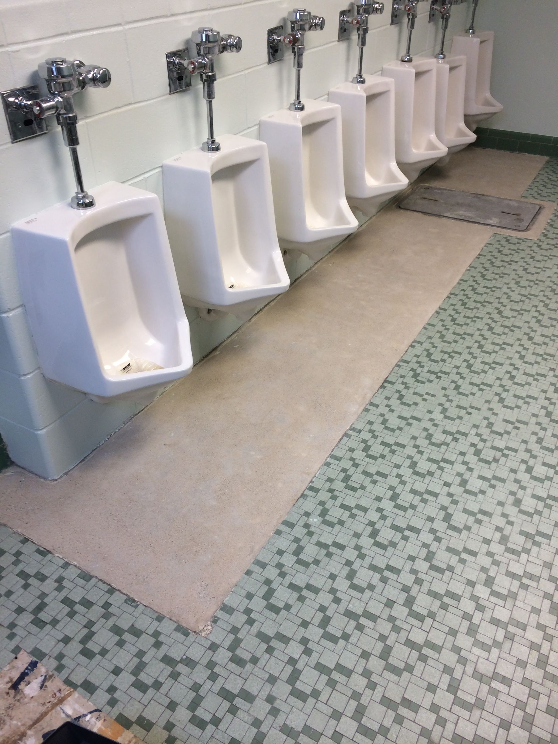 Row of white urinals with chrome flush valves in a tiled public restroom