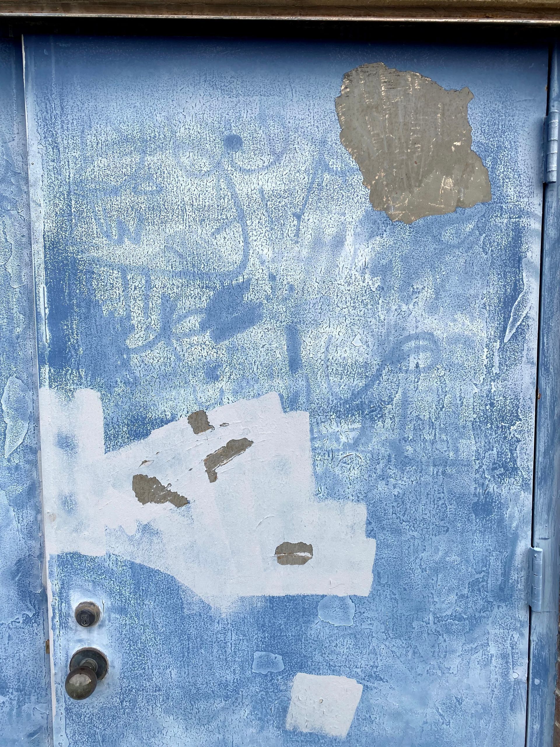 Weathered blue door with peeling paint, patches, and a handle on the left side