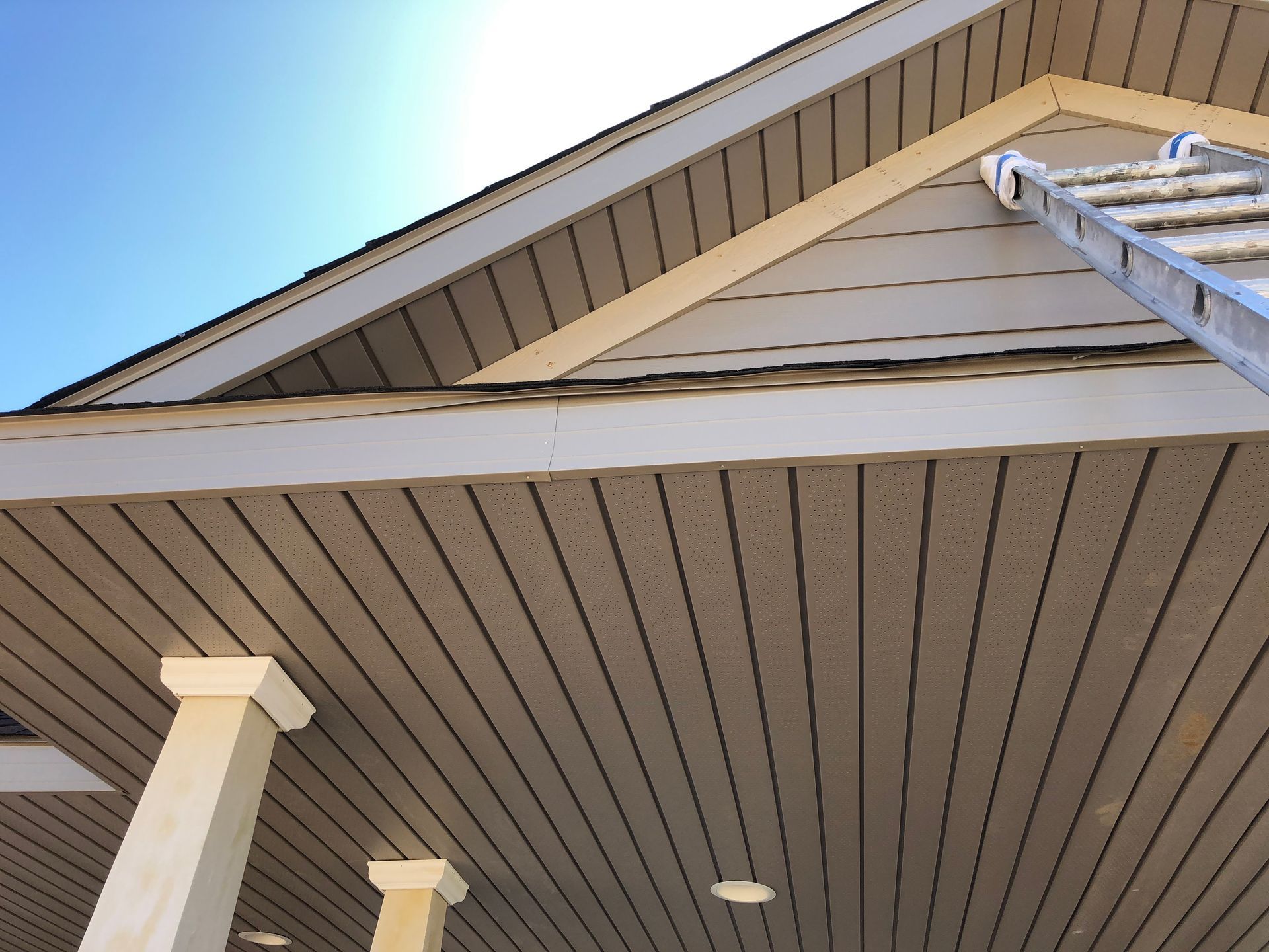 Close-up of a house roof and soffit with beige siding and a blue sky above