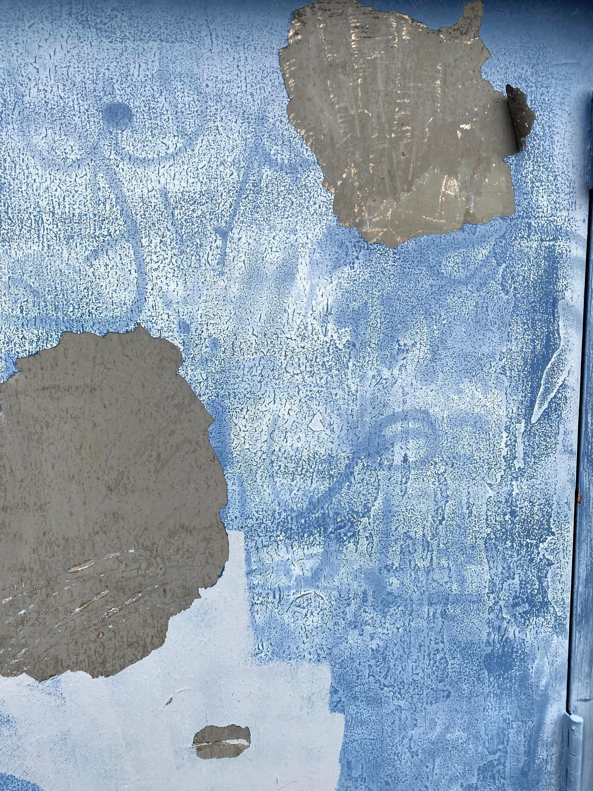 Peeling blue wall with exposed gray patches and weathered paint