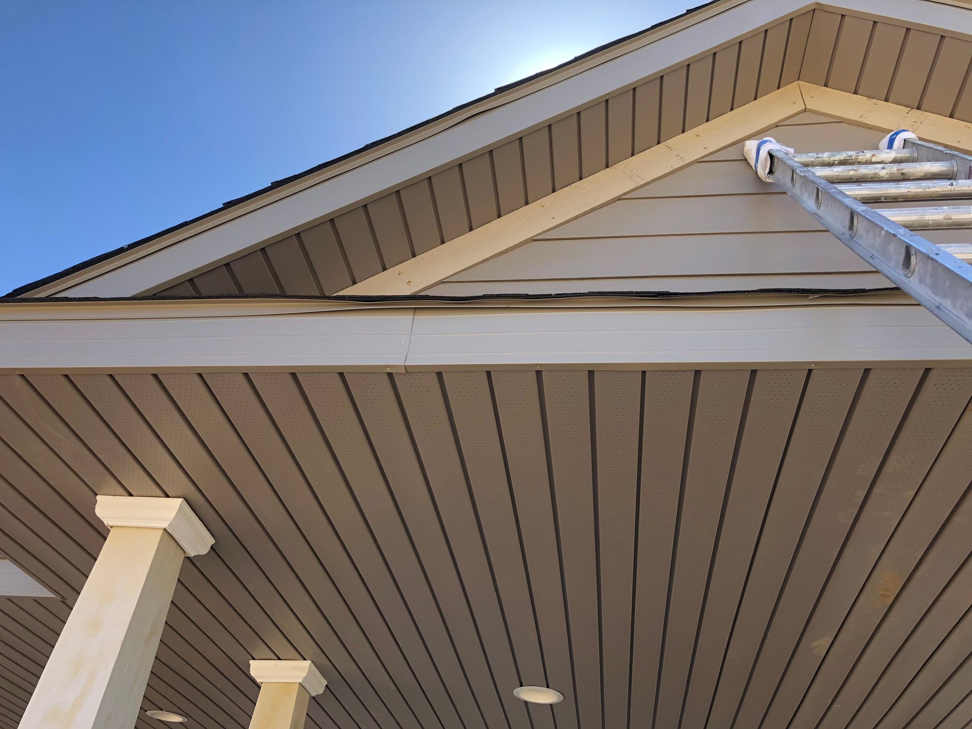 House roof eaves with tan siding and a ladder reaching the upper edge
