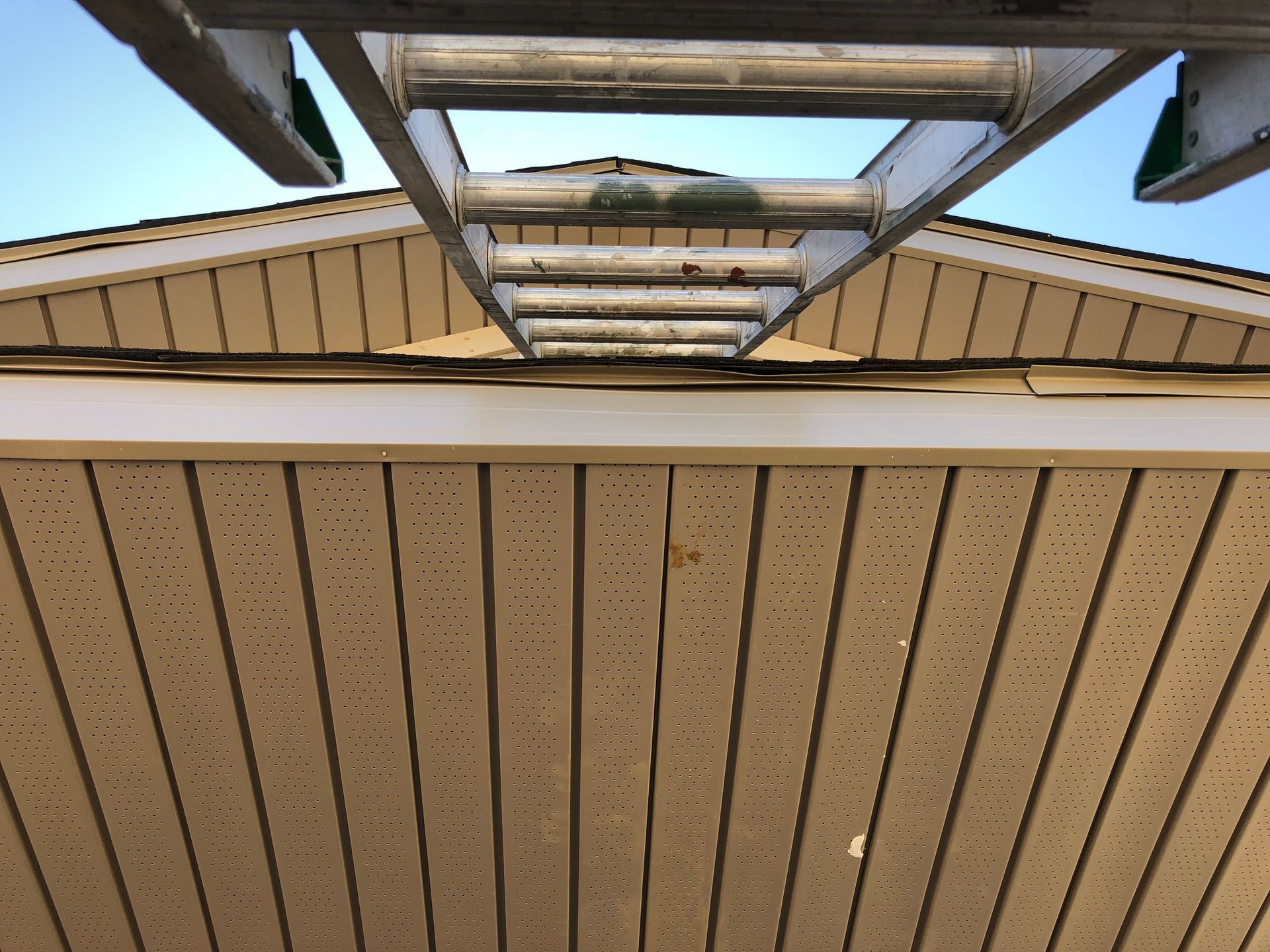 Close-up of a tan house exterior with a metal ladder extending above the roofline.