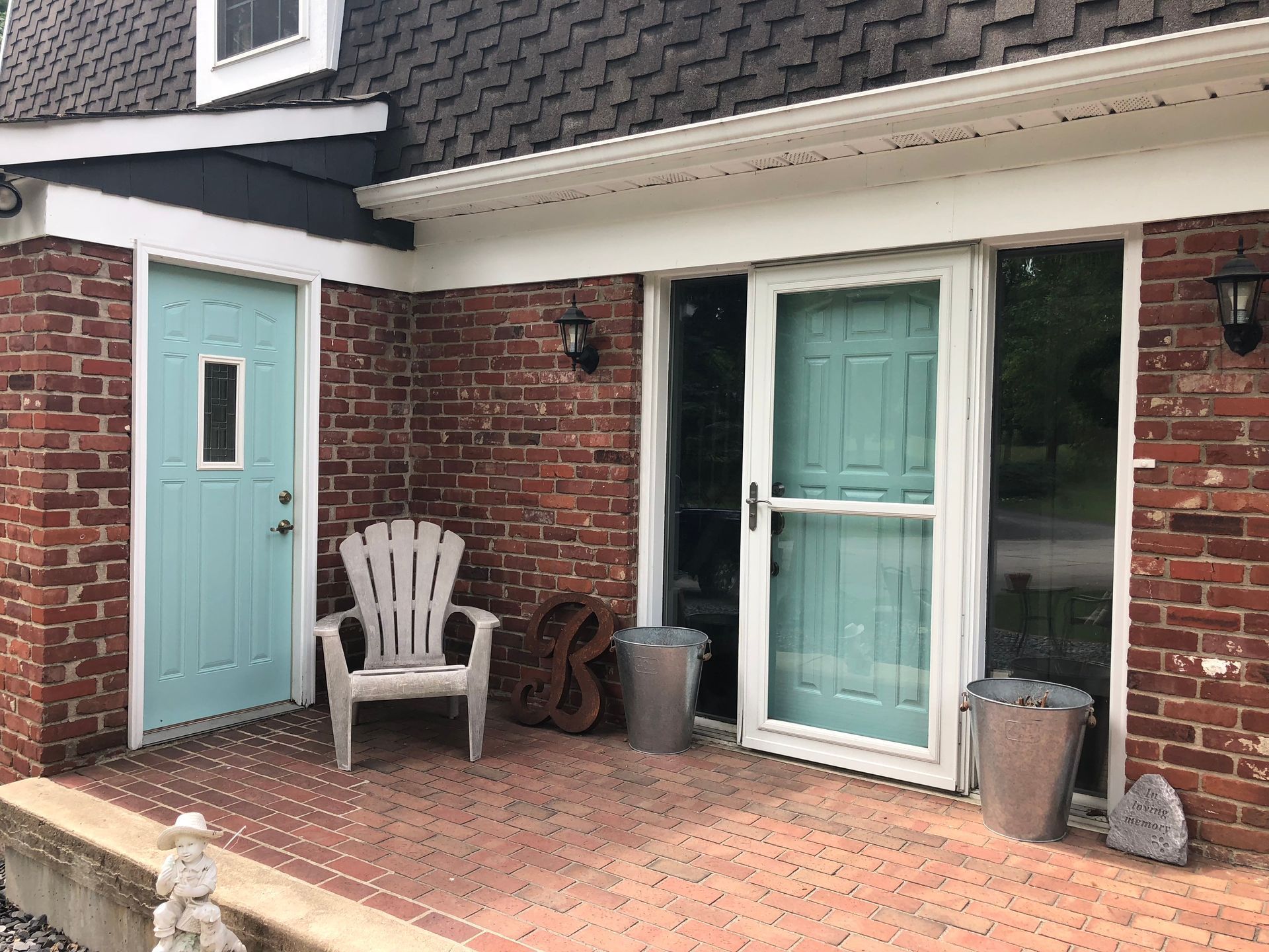 Front porch with teal doors, brick facade, white chair, and potted plants.