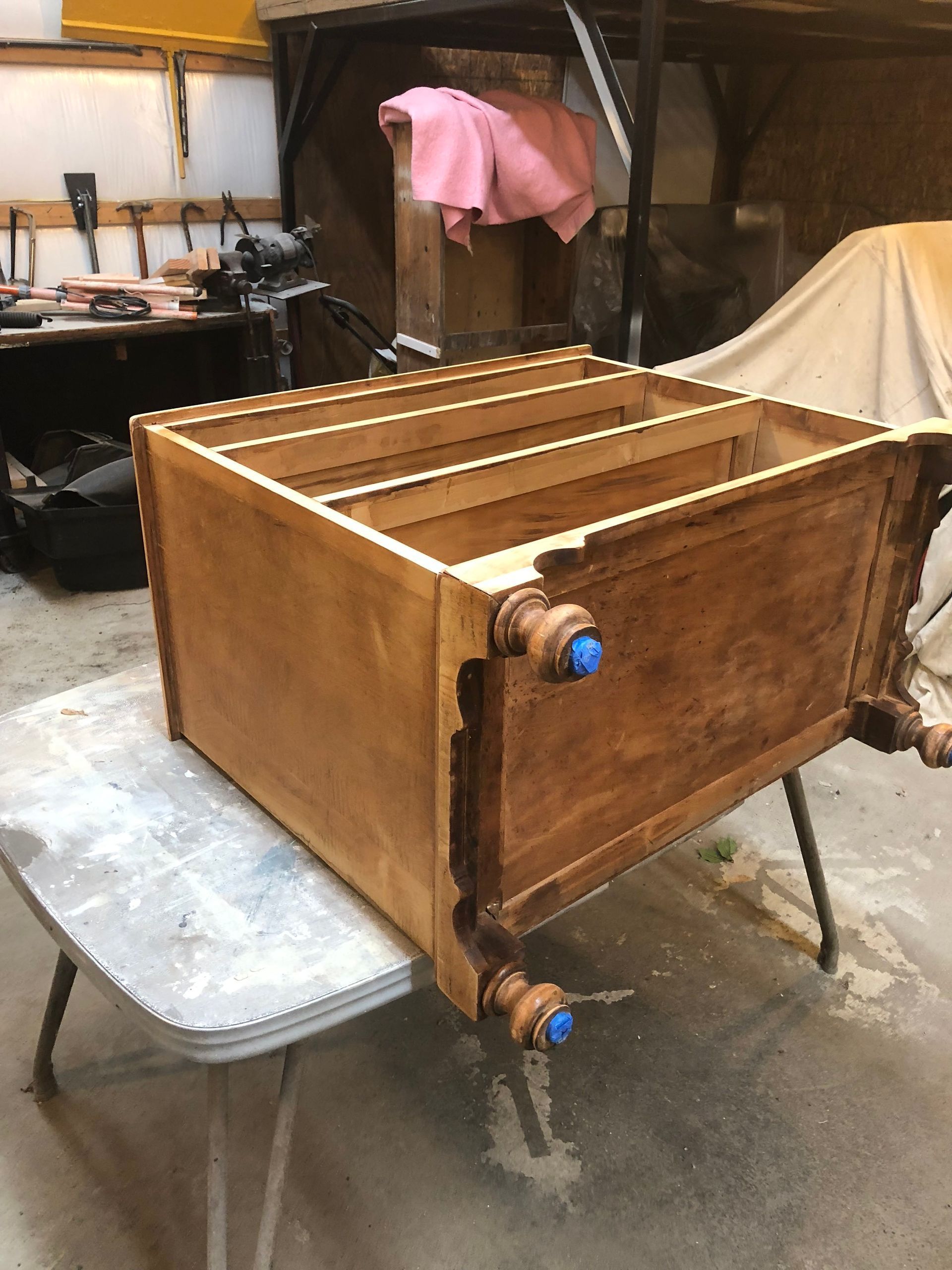 Wooden box on a workshop table with metal fittings and blue knobs, viewed from the side.
