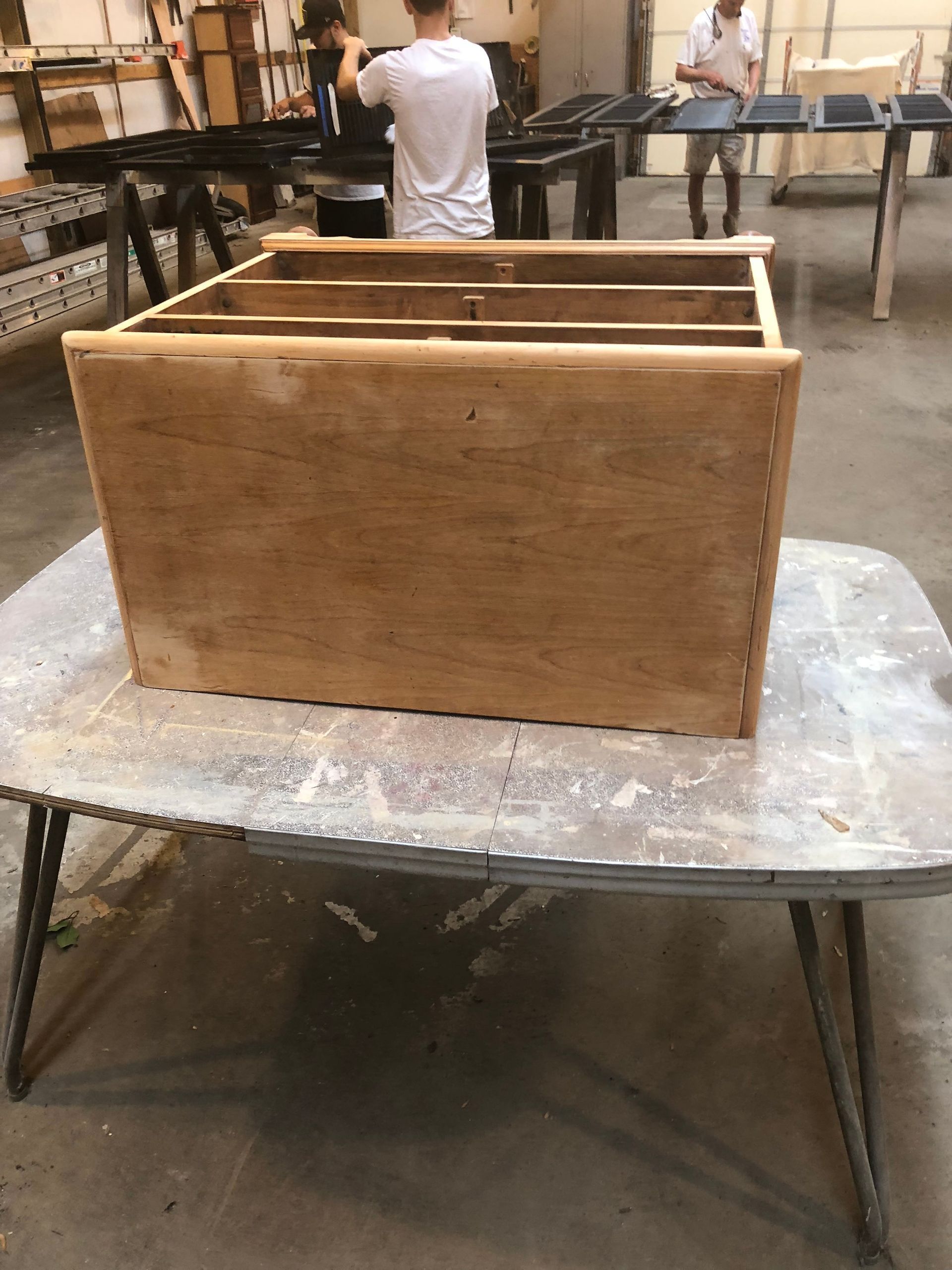 Wooden crate frame on a workbench in a workshop, with people blurred in the background.