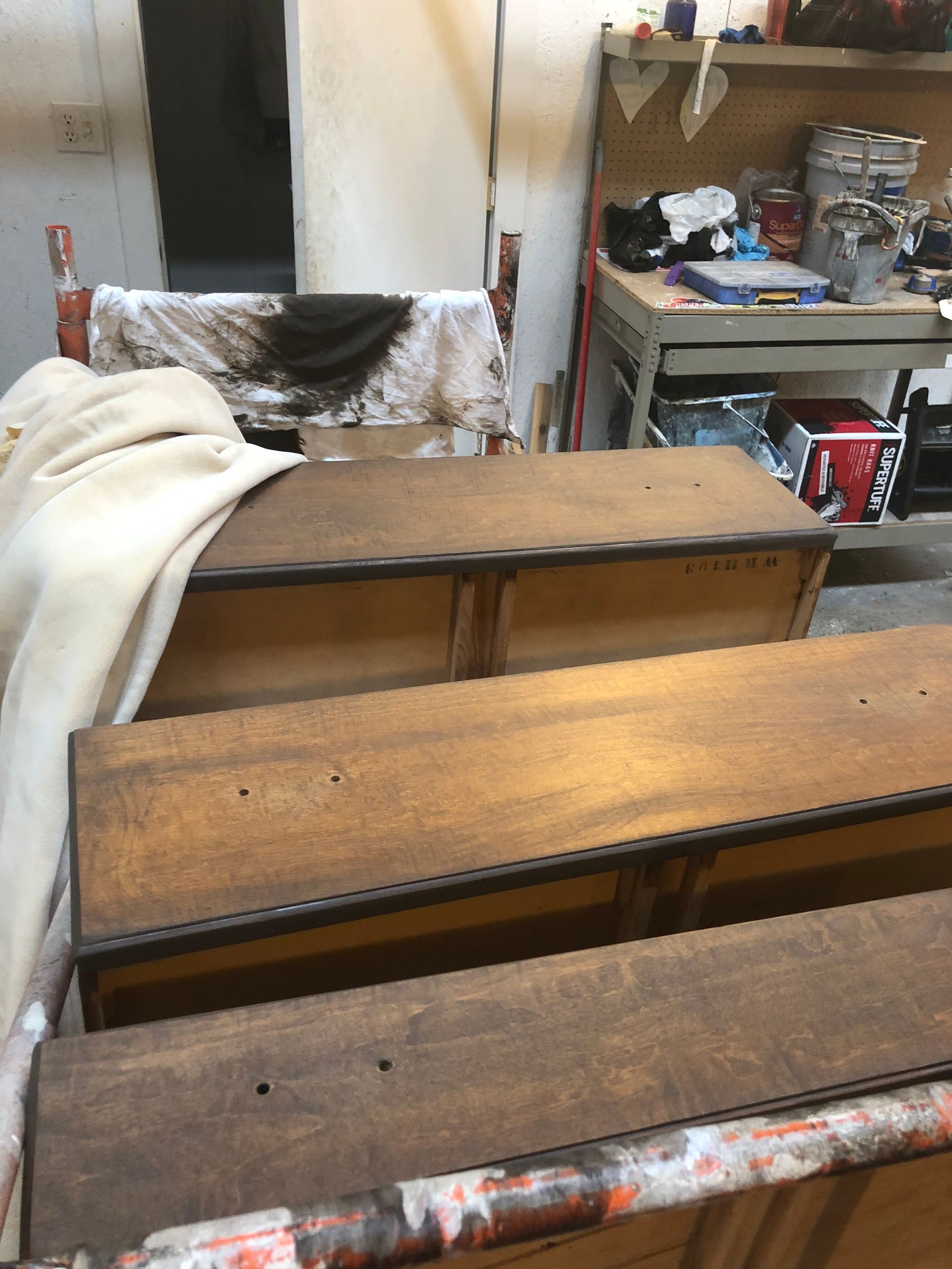 Wooden benches in a cluttered workshop with a white cloth draped over one side