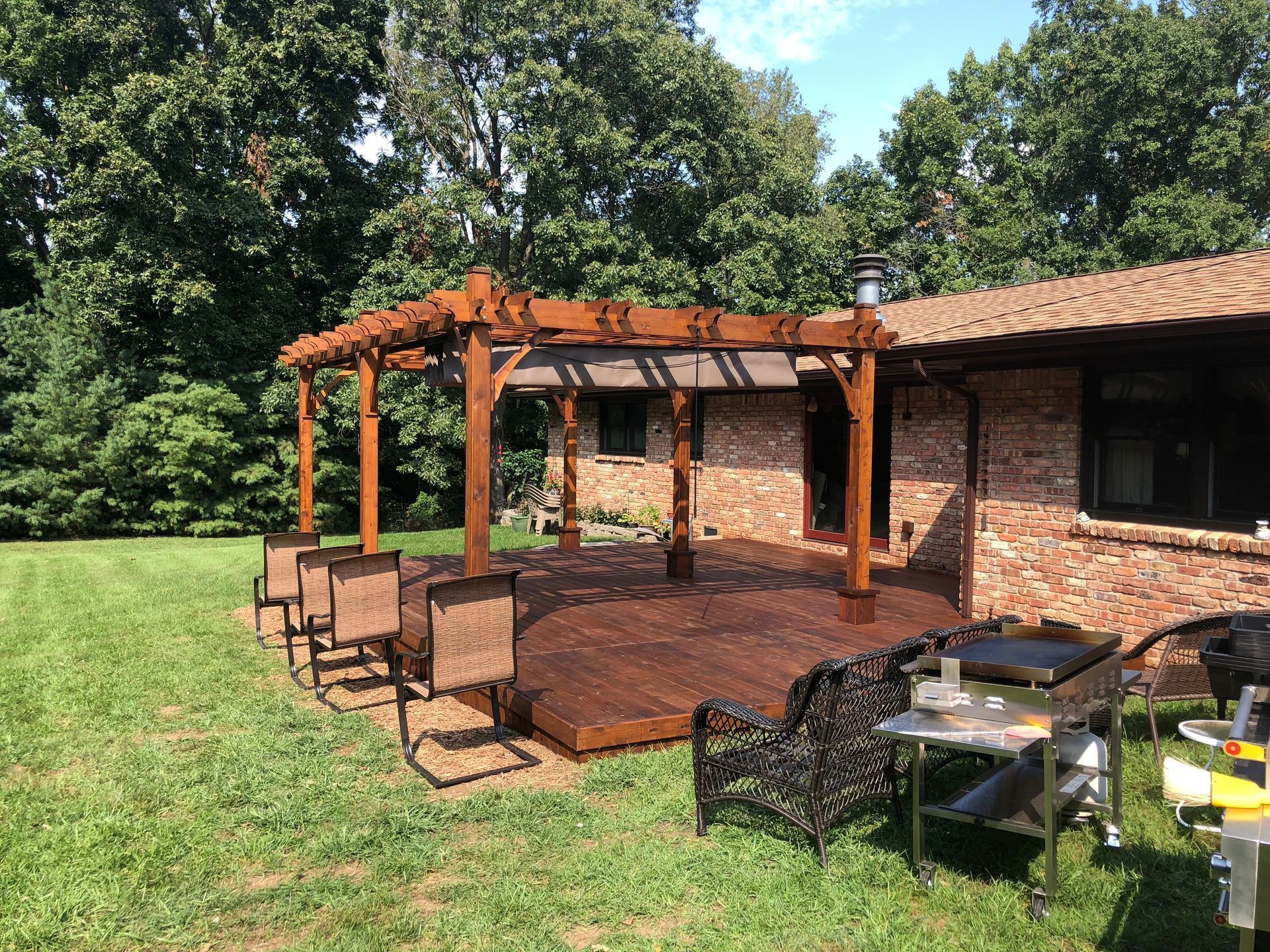 Brick patio with pergola, wicker chairs, and outdoor table beside a brick house and lawn