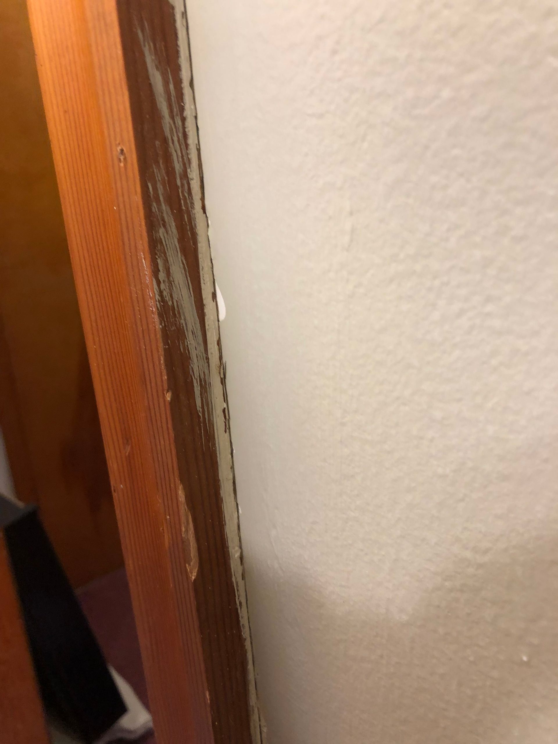 Close-up of a chipped wooden door frame beside a beige wall.