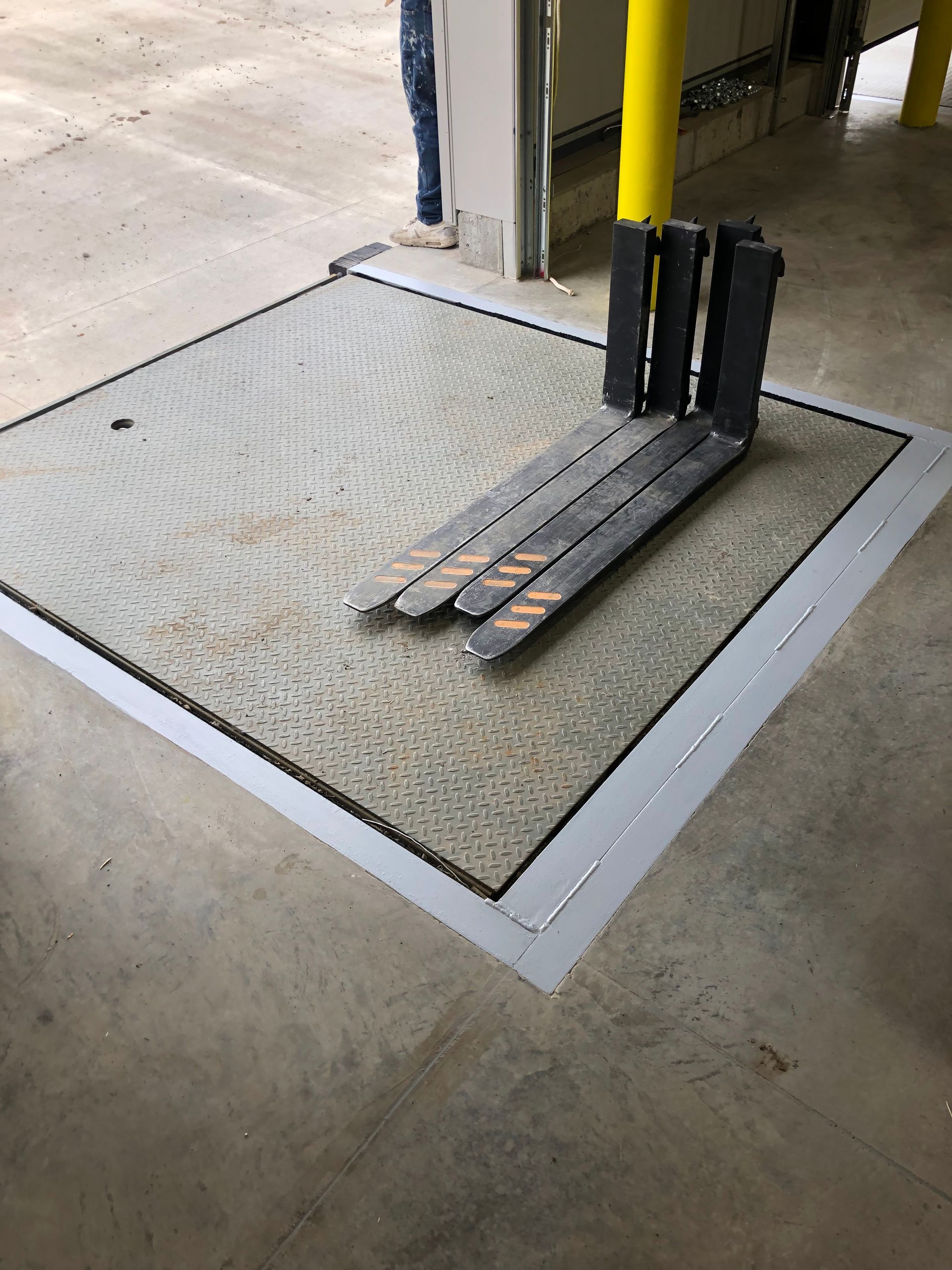 Hand truck with yellow handle on a textured mat over a recessed floor platform in a warehouse setting