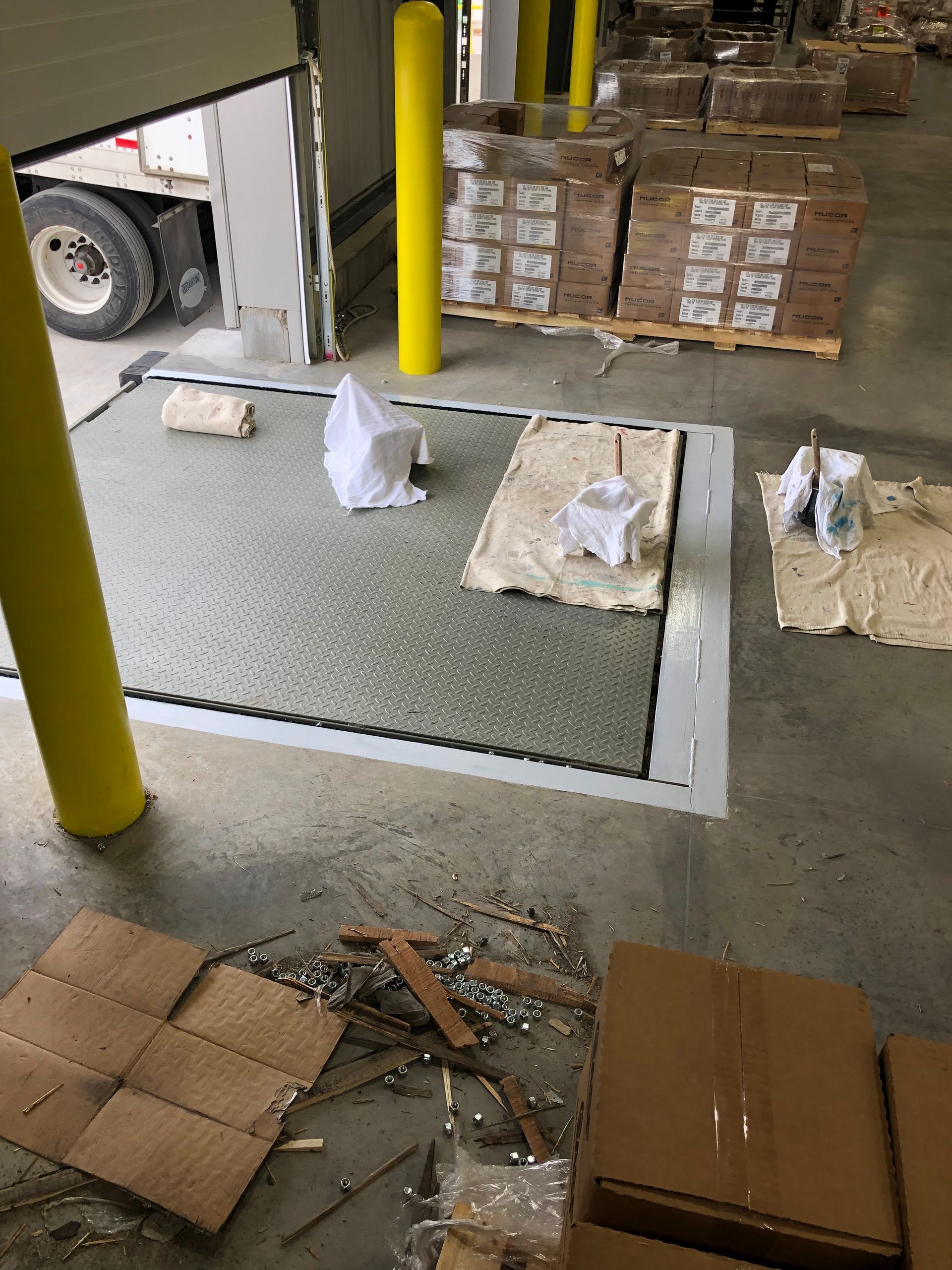 Warehouse floor with scattered debris, cardboard boxes, and wrapped items near a loading area.