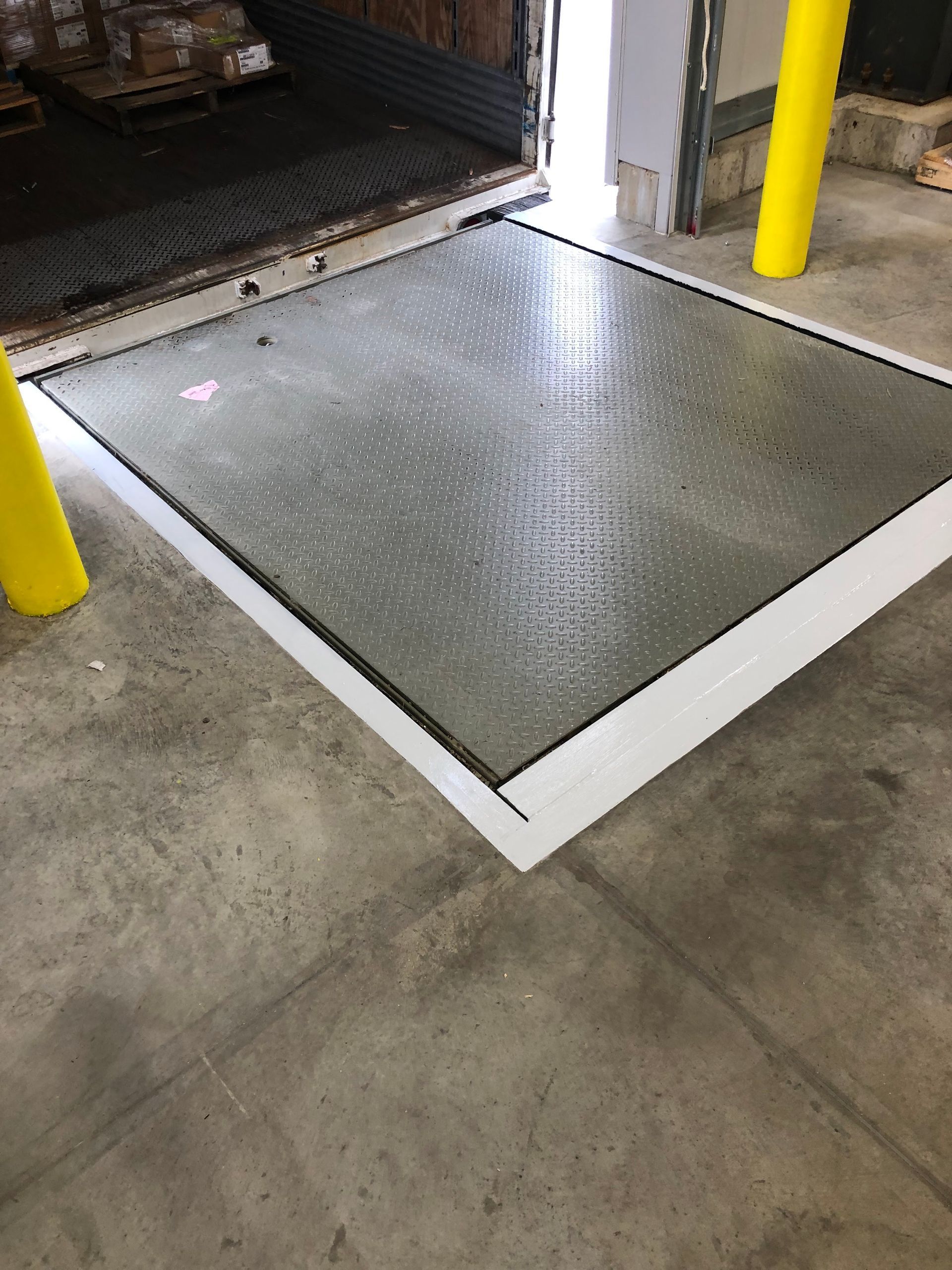 Industrial loading dock with a metal platform and yellow safety bollards on a concrete floor