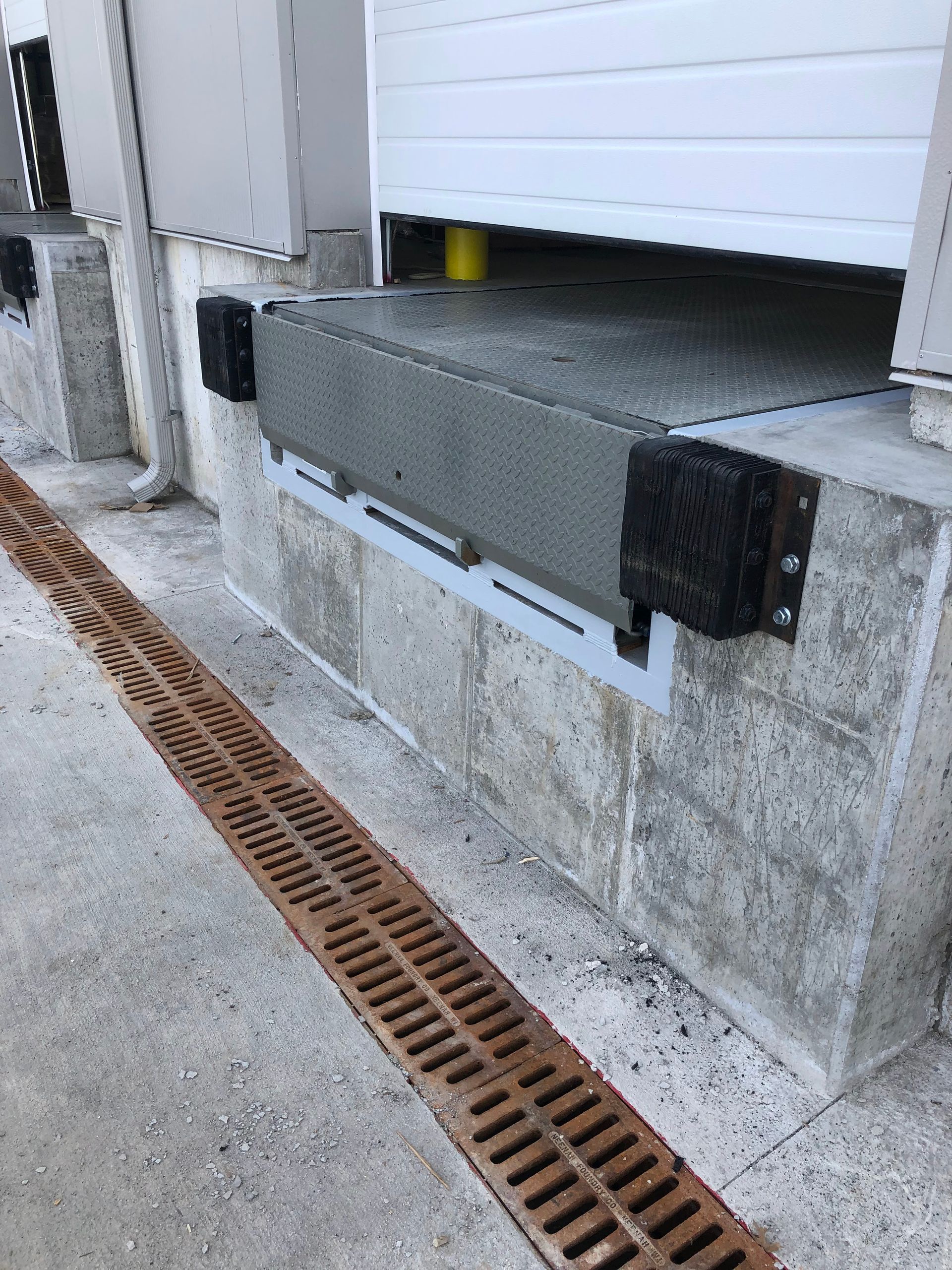 Loading dock with a gray bumping dock and a closed white garage door above a drainage grate