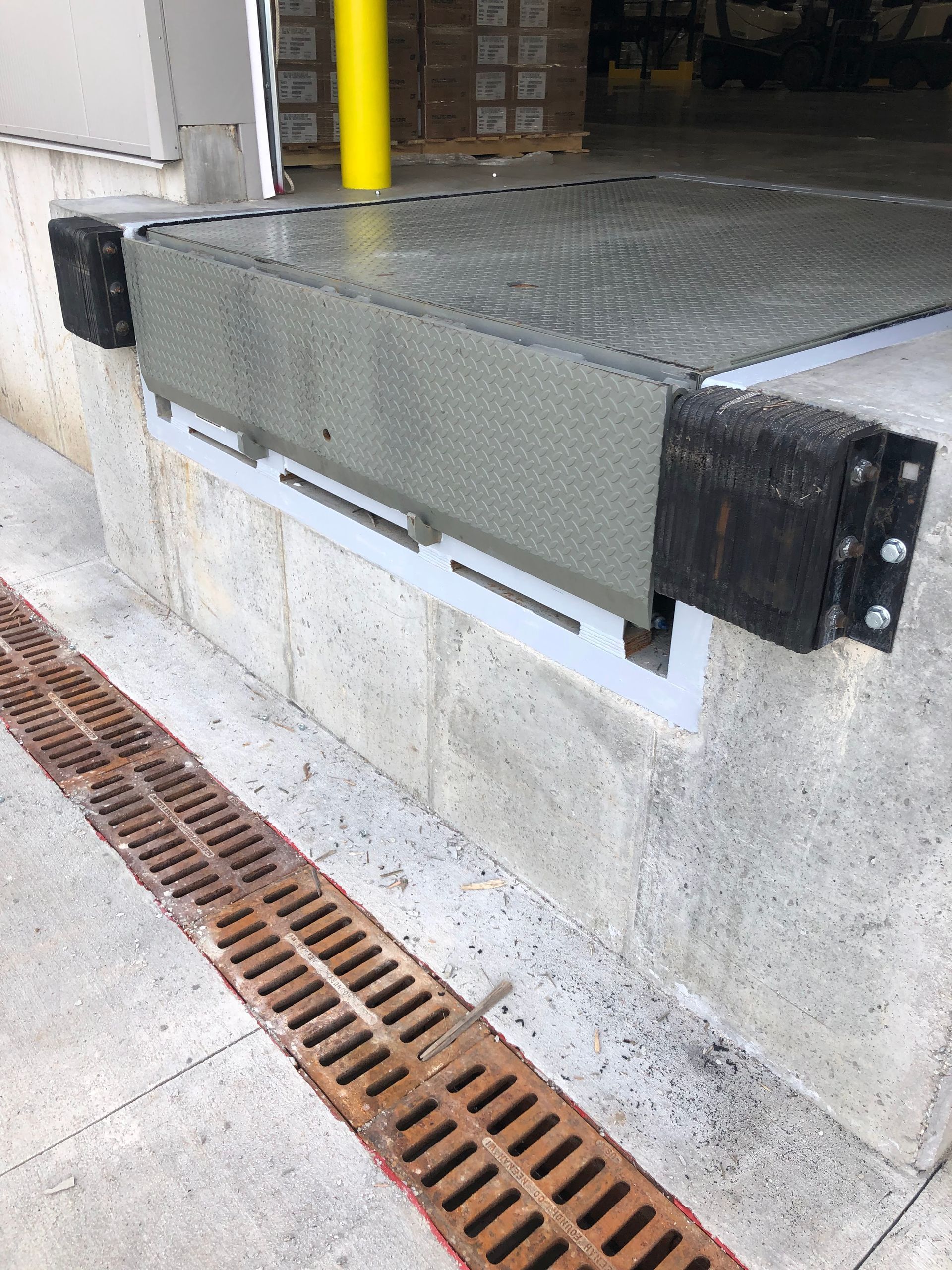 Elevated metal platform over concrete with a yellow pipe and drainage grate below