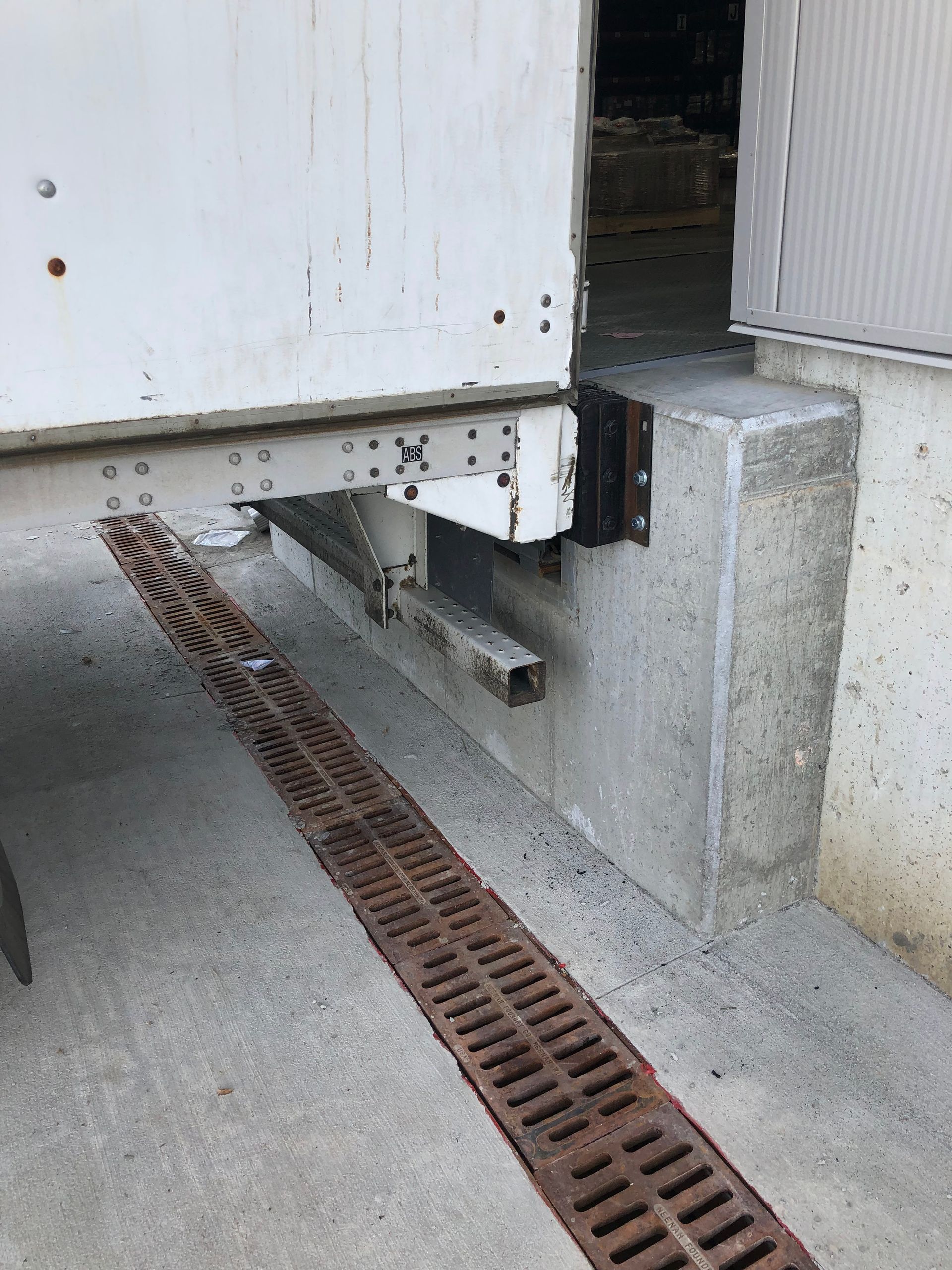 White metal structure on concrete blocks beside a grated trench drain outdoors.