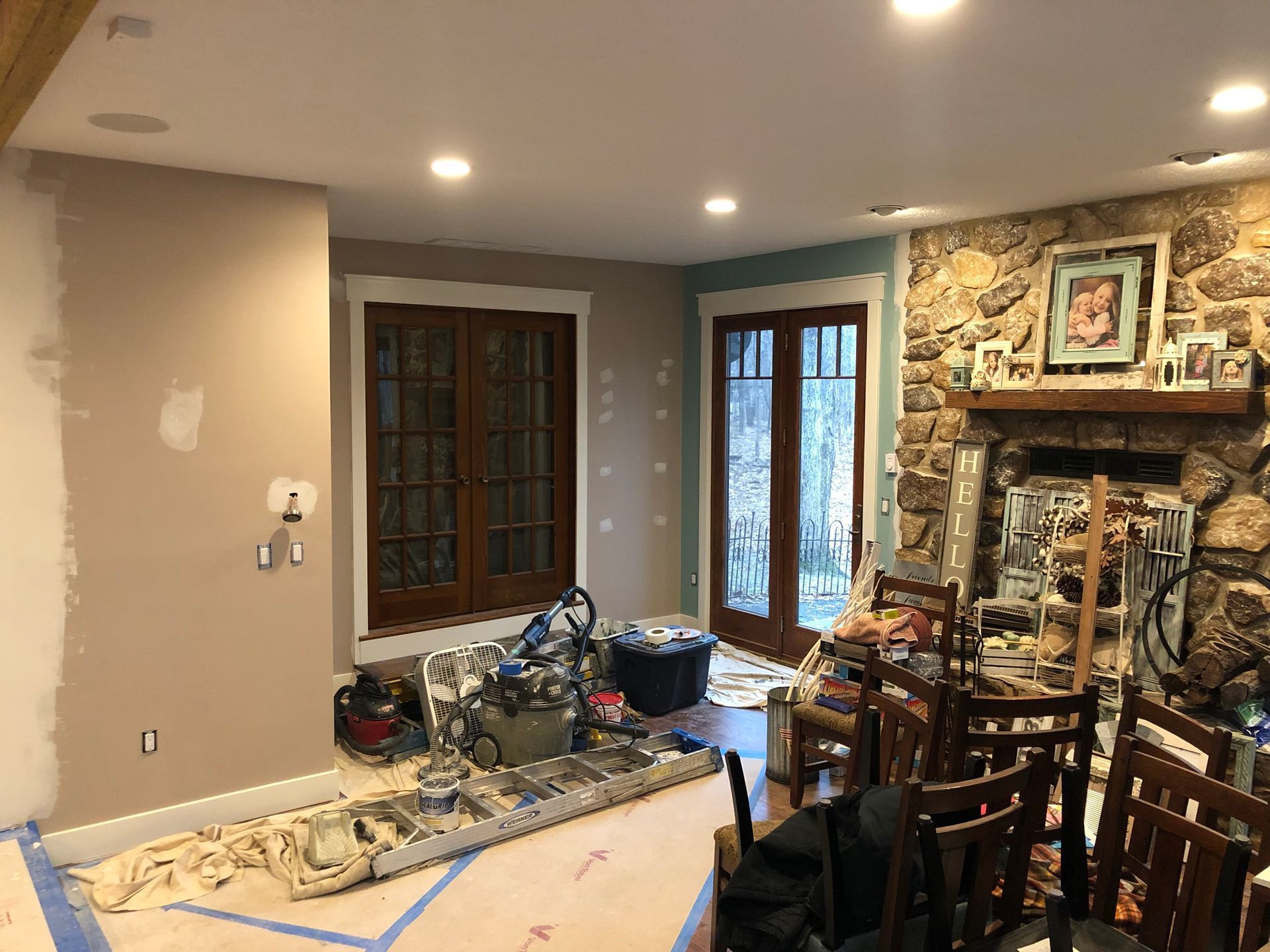 Living room under renovation with tools, covered furniture, and a stone fireplace in the background