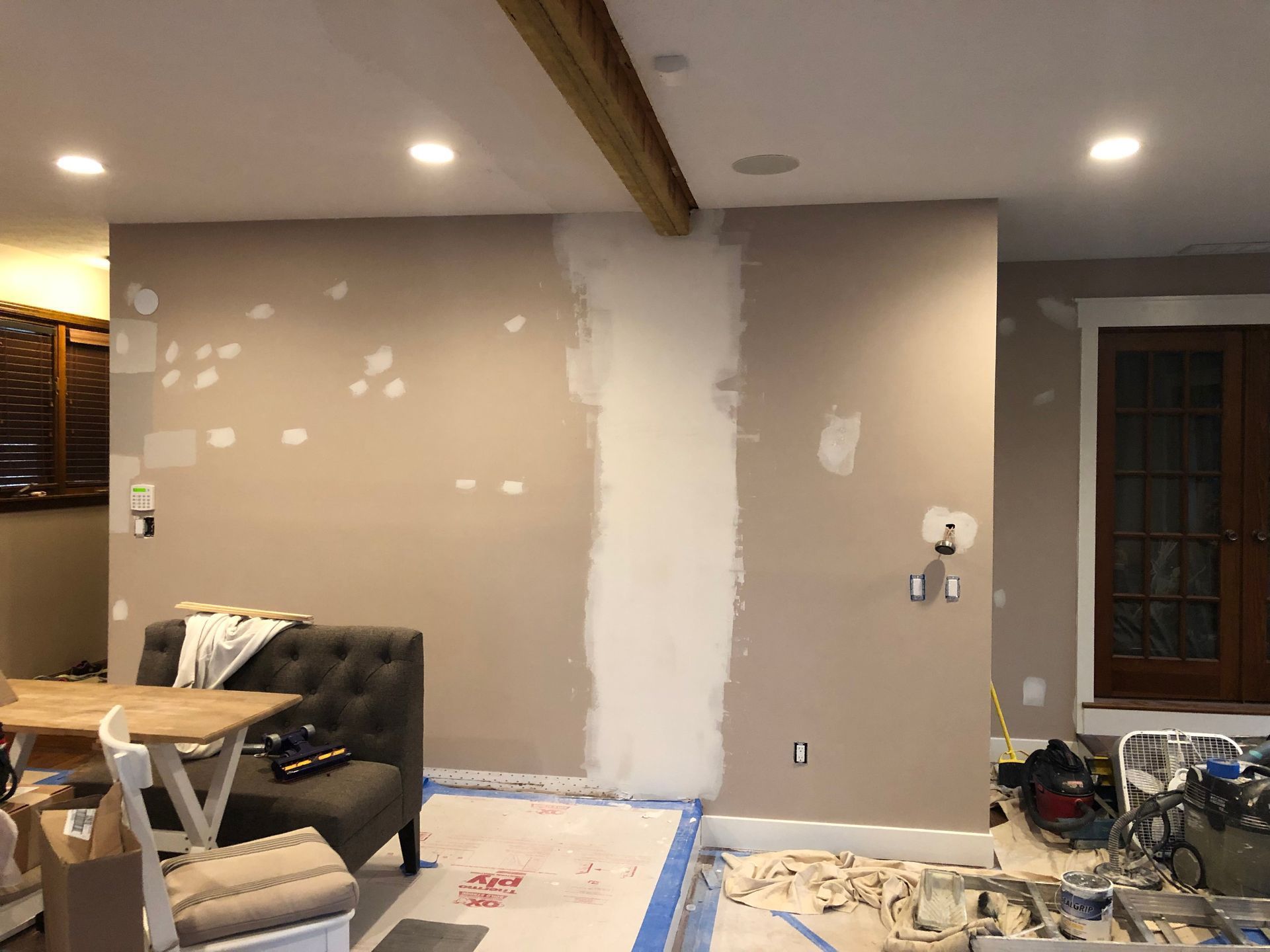 Partially renovated living room with taped drywall patch, couch, ladder, and tools on the floor