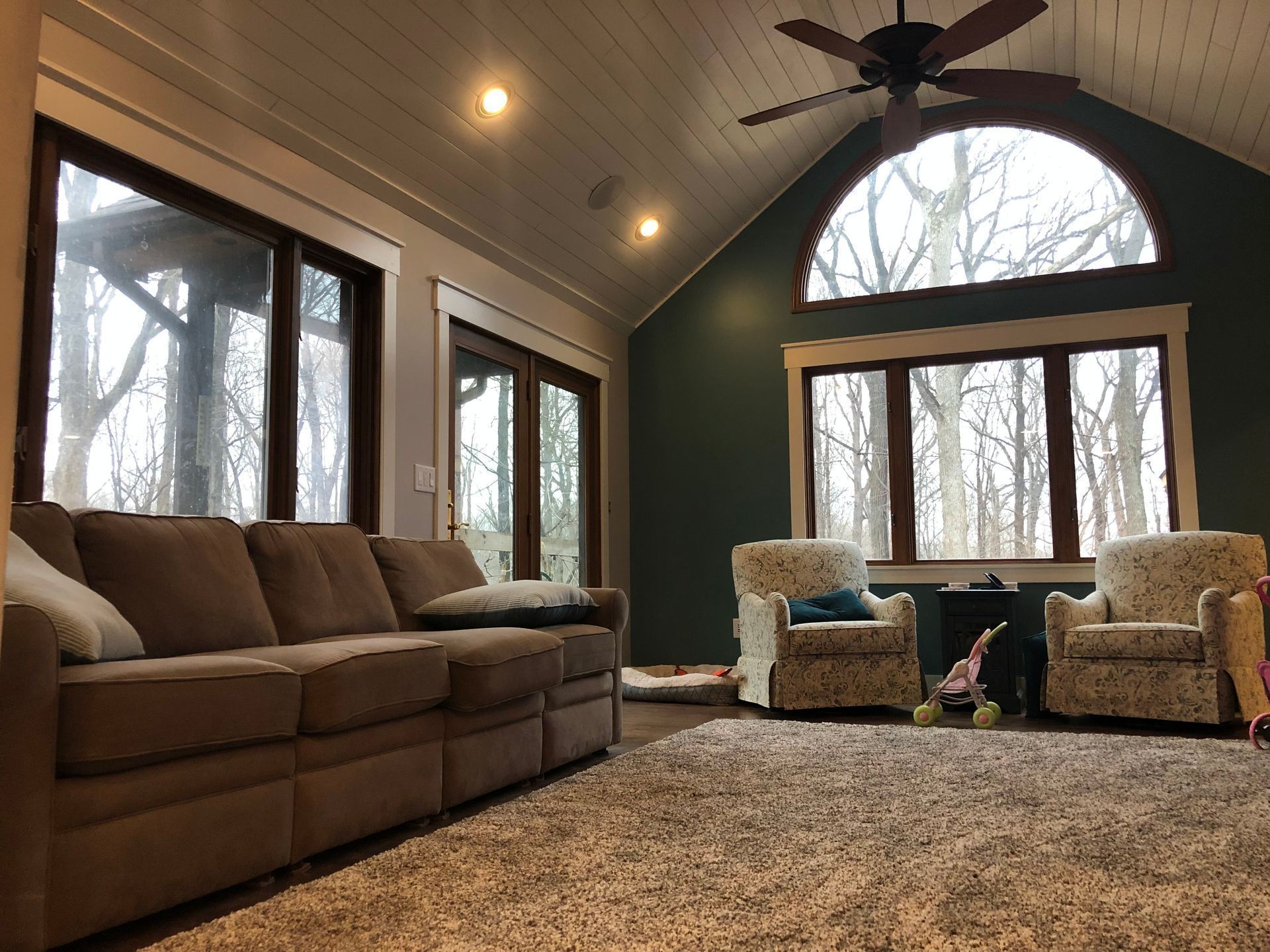 Cozy living room with brown sofa, two armchairs, large windows, and vaulted ceiling fan