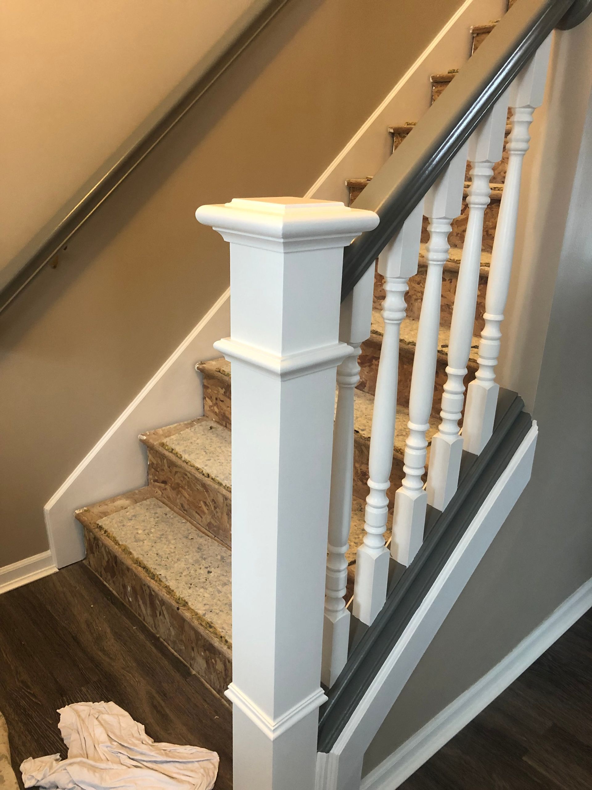 Staircase with beige carpeted steps, white banister, and dark wood floor beside gray walls