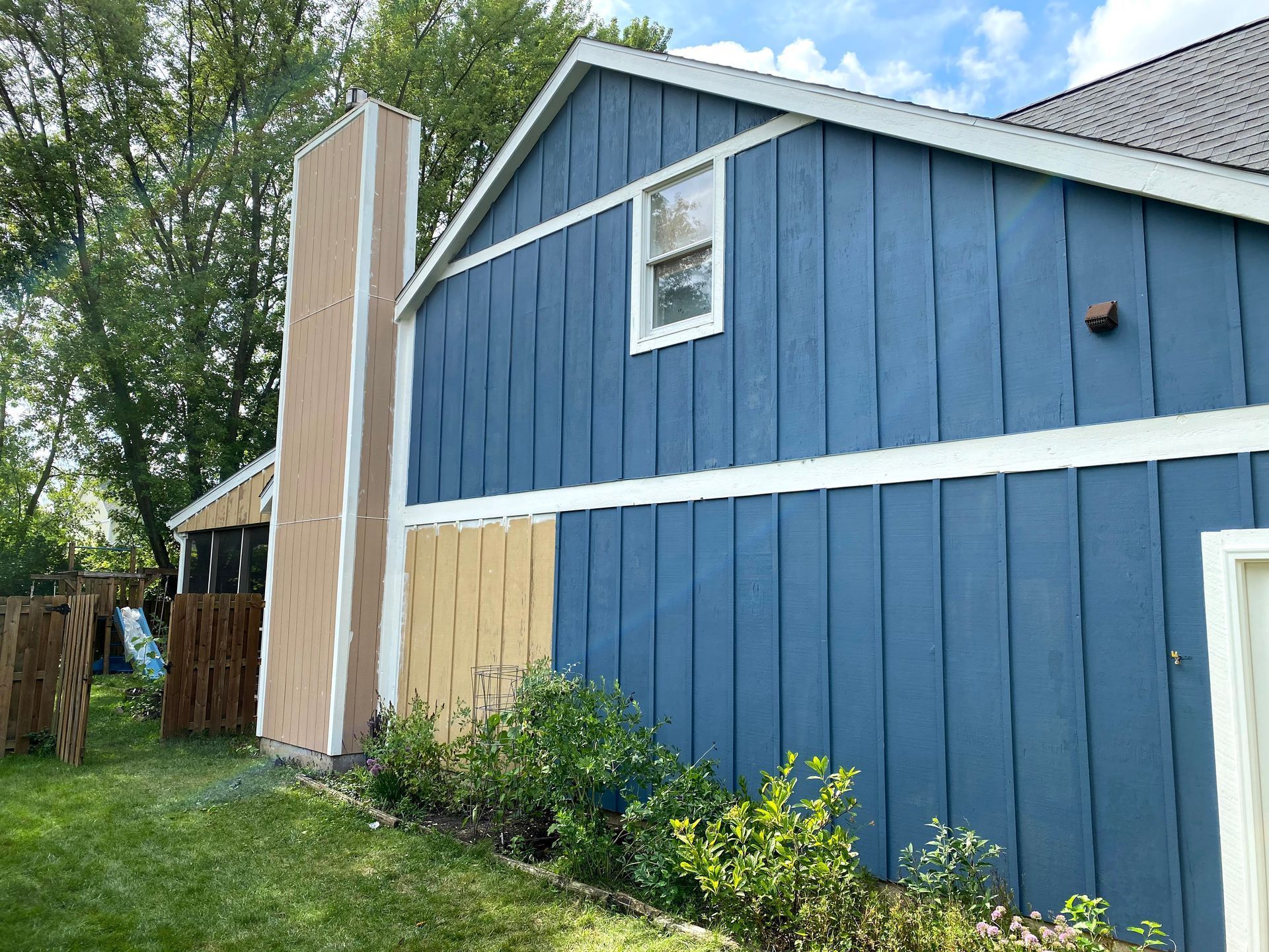 Blue house exterior with white trim and a tall brick chimney, beside a grassy yard and trees.