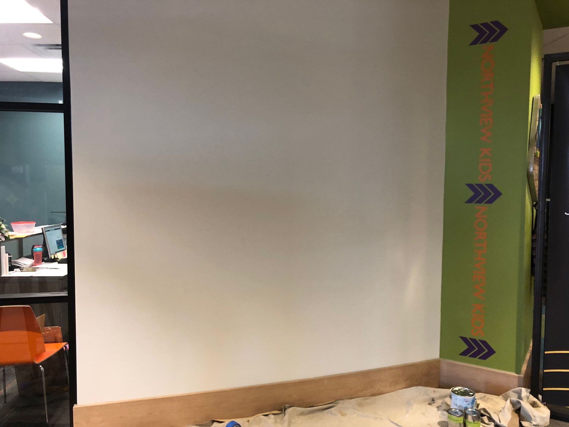 Empty white wall with wood trim, next to a green striped pillar and an office window