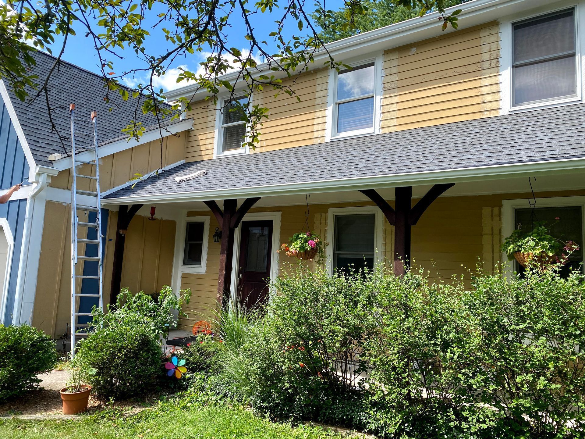 Two-story yellow house with a covered porch and lush front garden shrubs