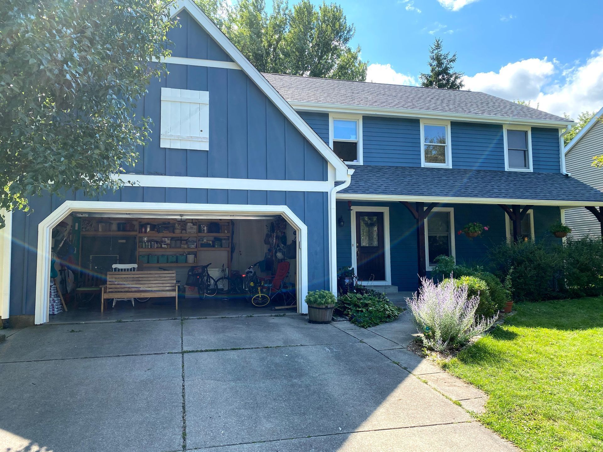Blue two-story house with open garage, driveway, and front porch in bright sunlight
