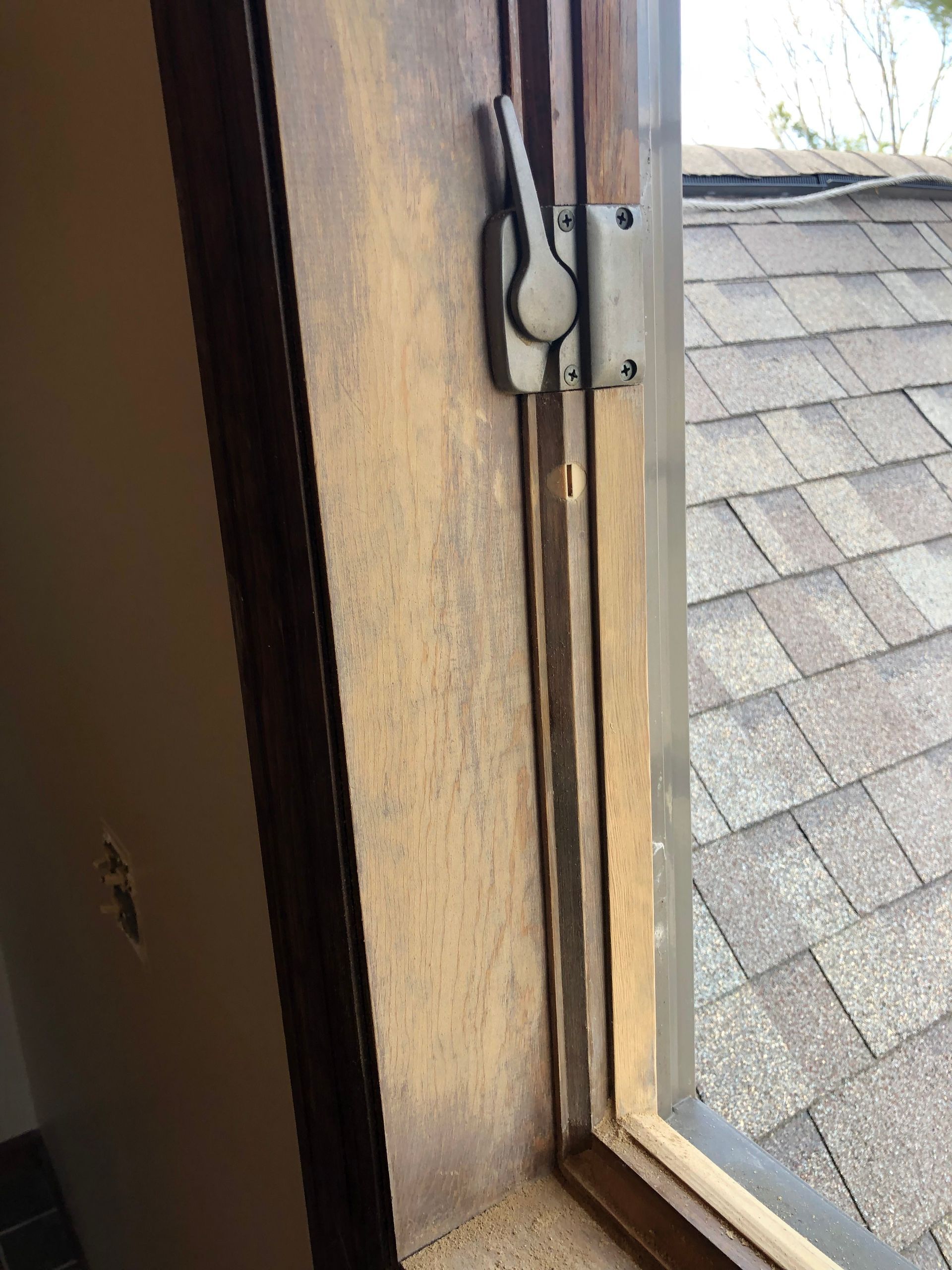 Open window with metal latch, looking out at gray shingled roof and bright sky.