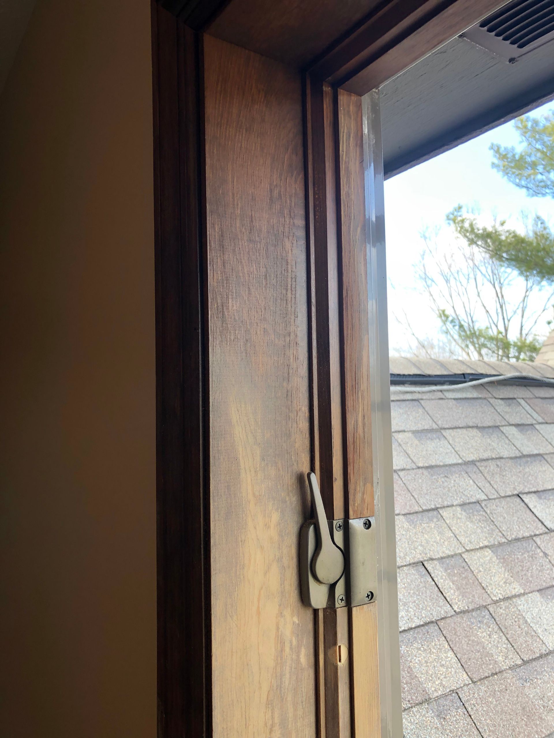 Wooden window latch on an open window frame with rooftop and trees visible outside