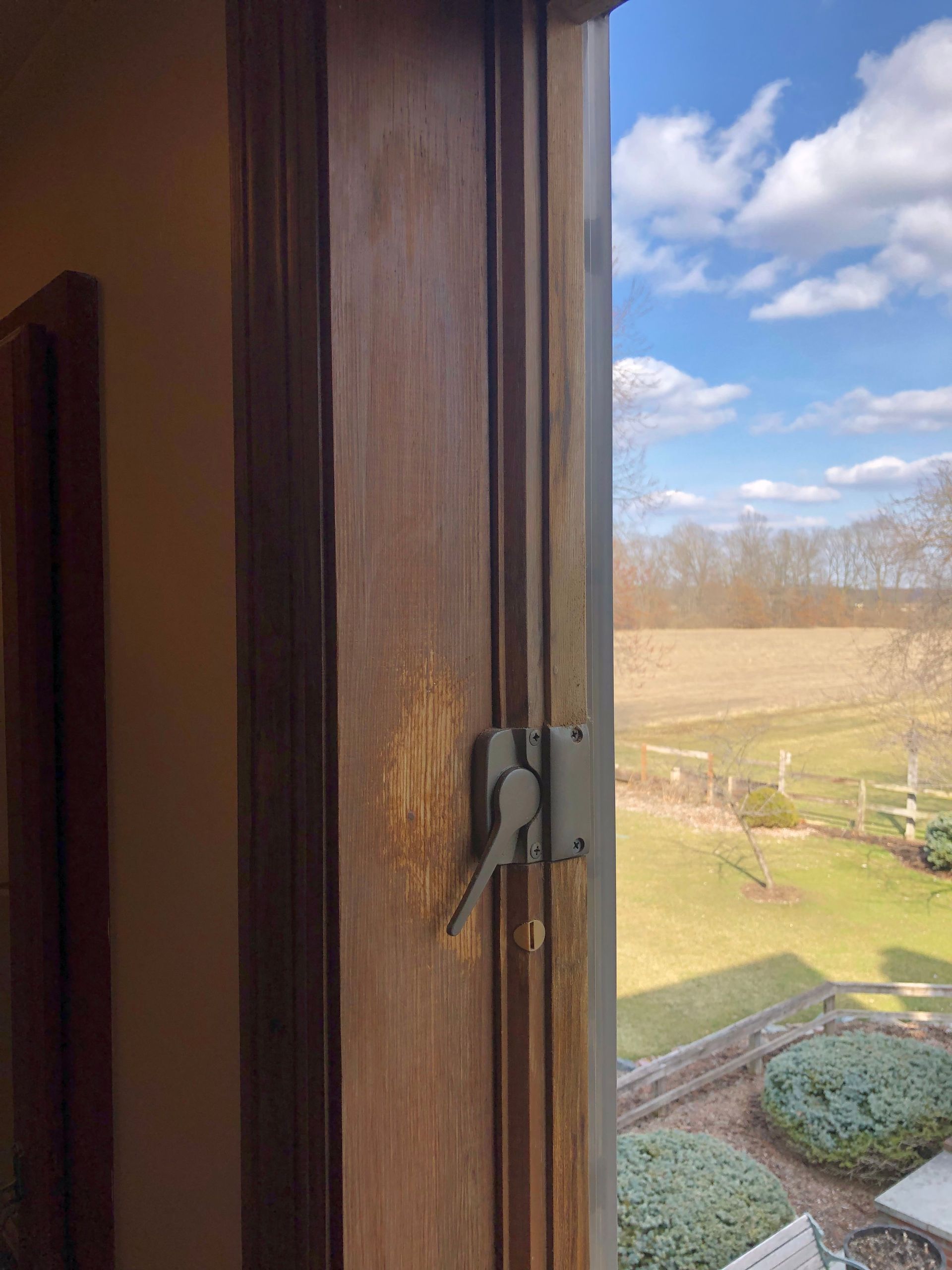 Wooden window frame with latch, overlooking a sunny field and blue sky.
