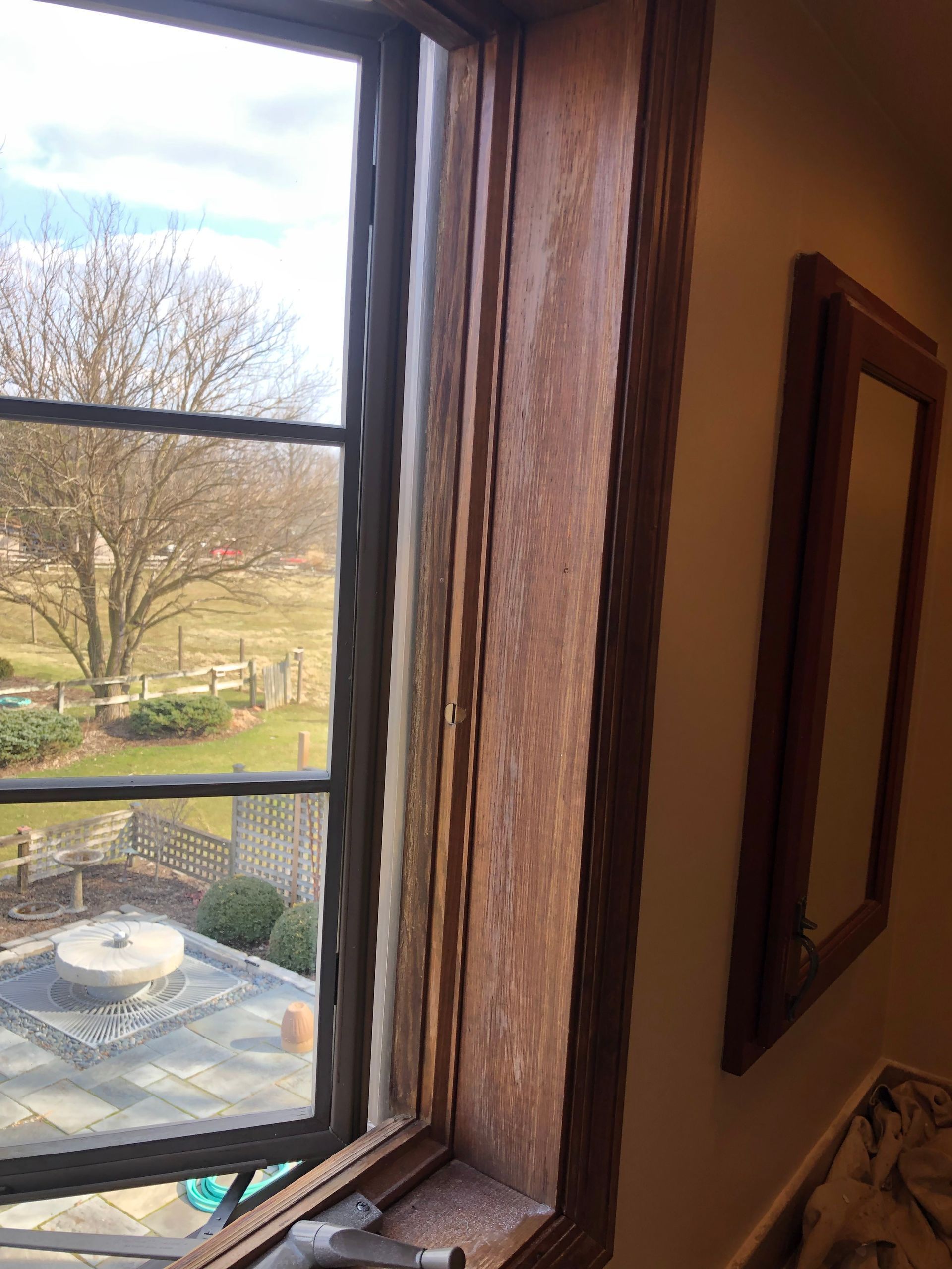 View through a window to a courtyard with trees and a patio table; wall mirror on the right.